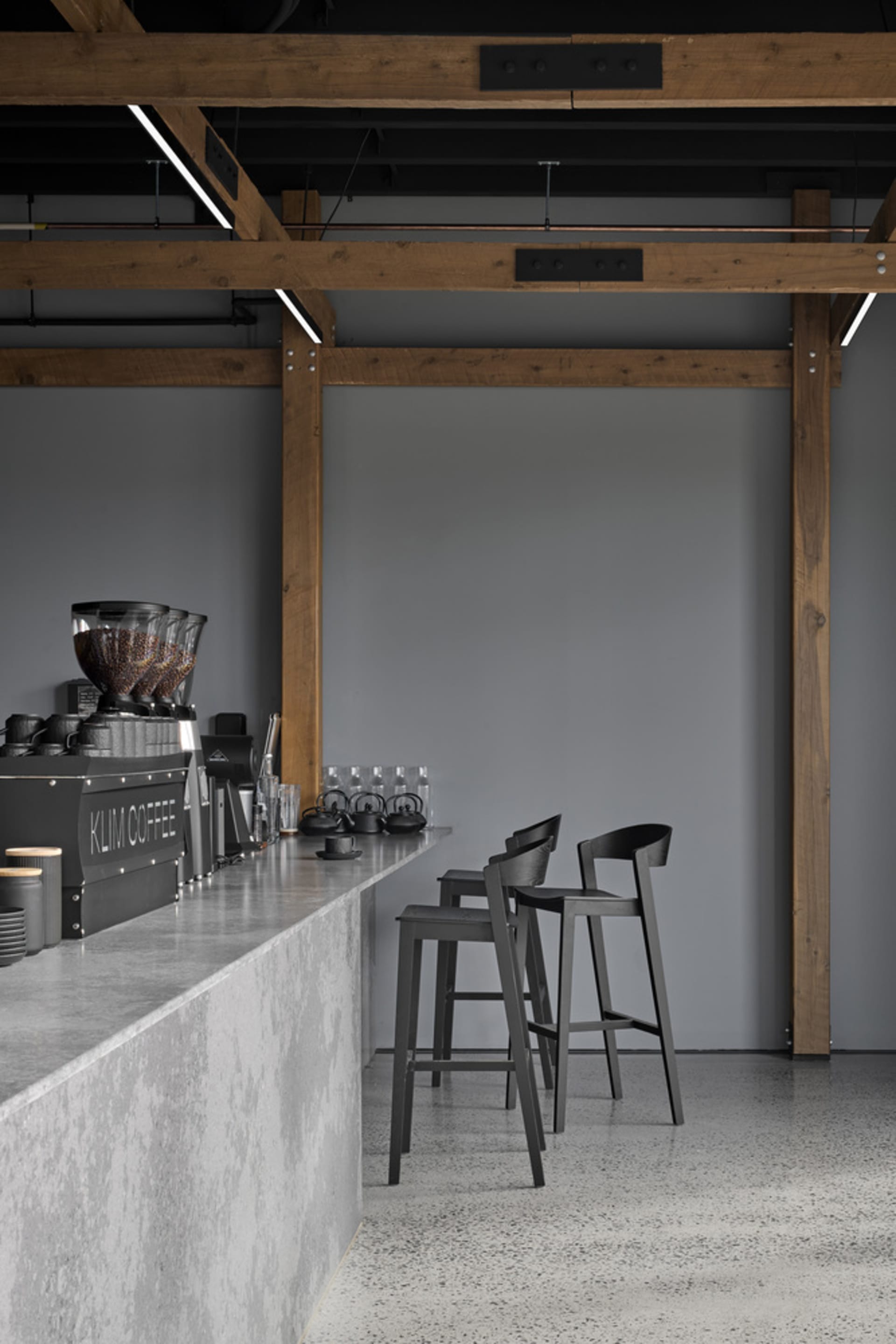 A minimalist industrial-style coffee shop bar with concrete countertops, wooden beams, and metal furniture.