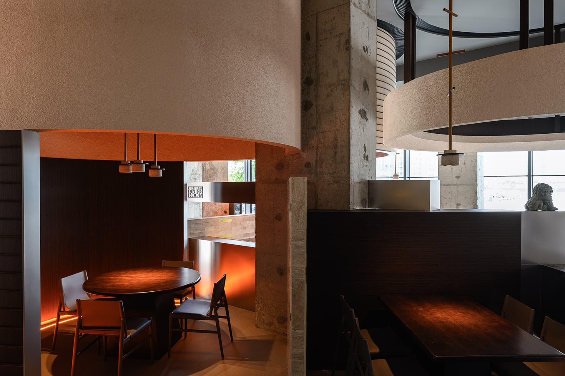 Modern industrial restaurant interior with wooden tables and chairs, concrete walls, and circular pendant lights.