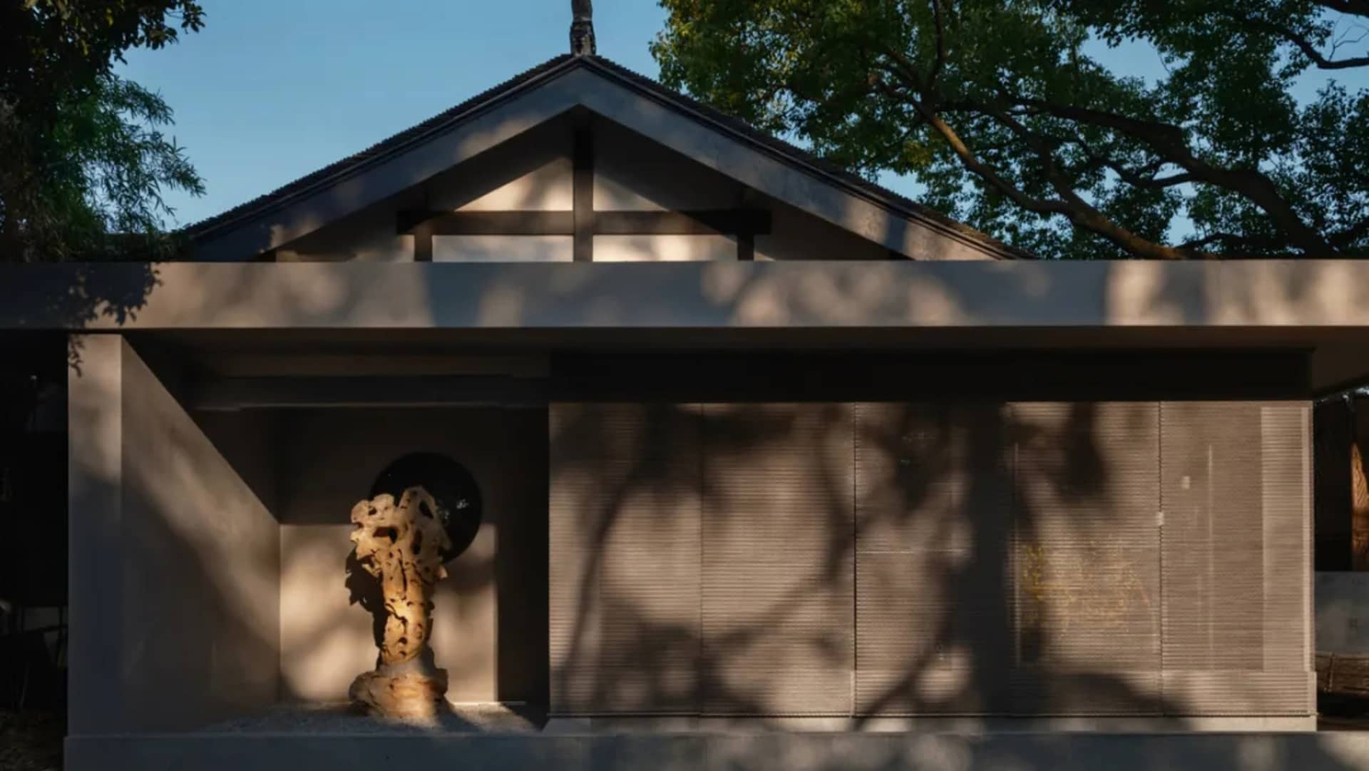 A modern house with a concrete exterior and a tree casting shadows on the wall.