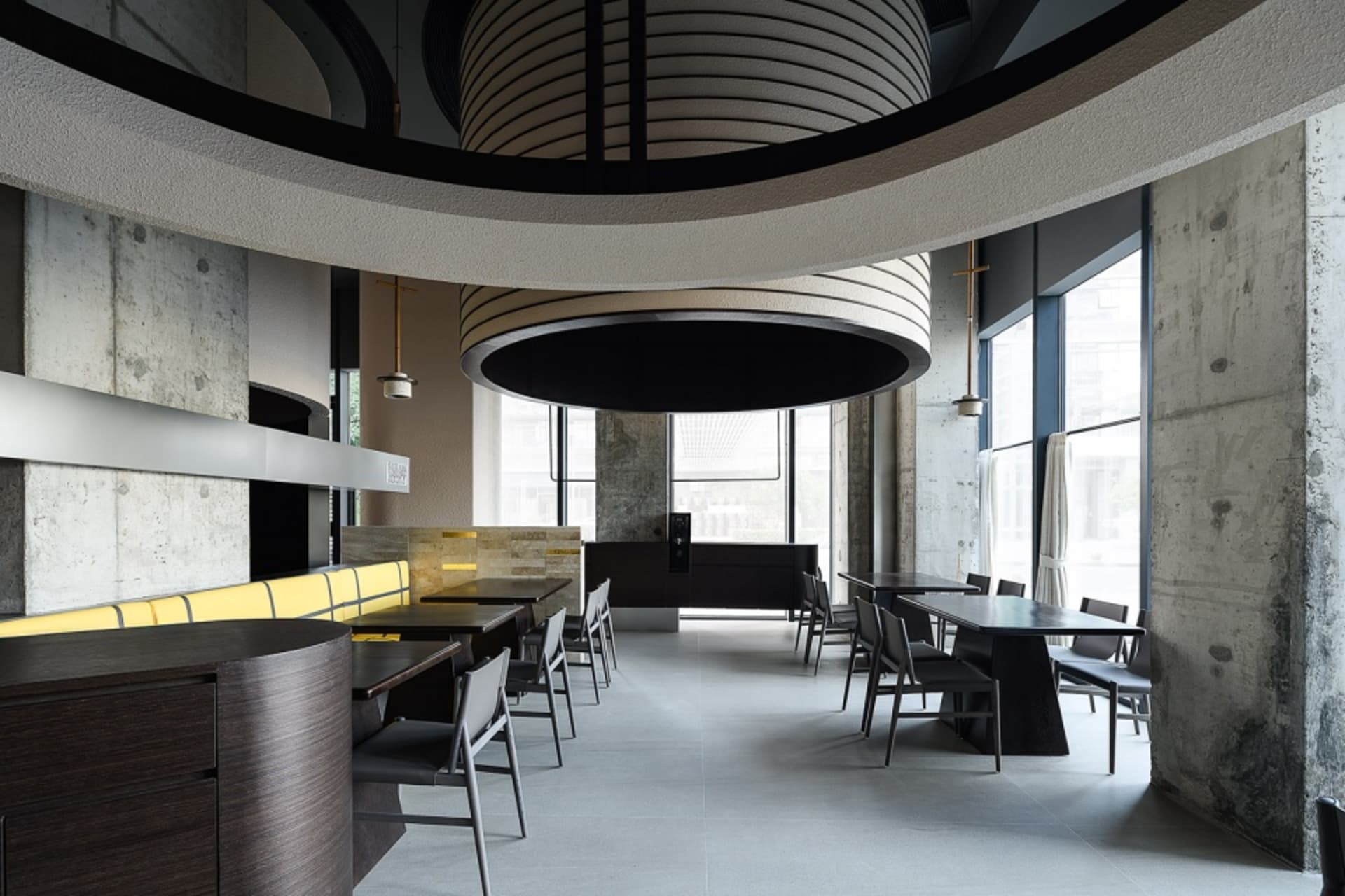 Modern restaurant interior with concrete walls, wooden furniture, and large windows.