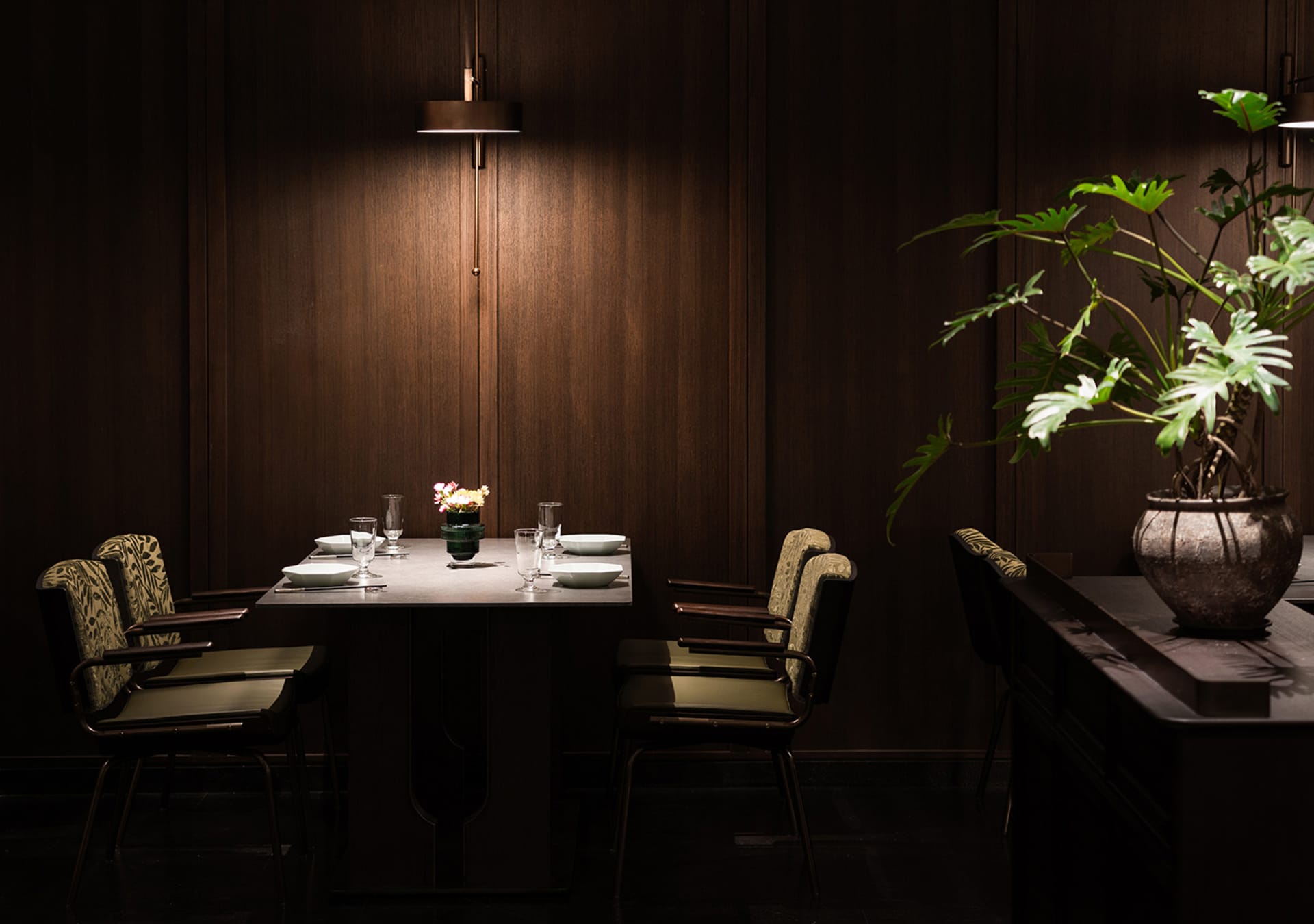 現代餐廳室內,深色木質牆面與家具,餐桌為四人設置,配有白色餐盤