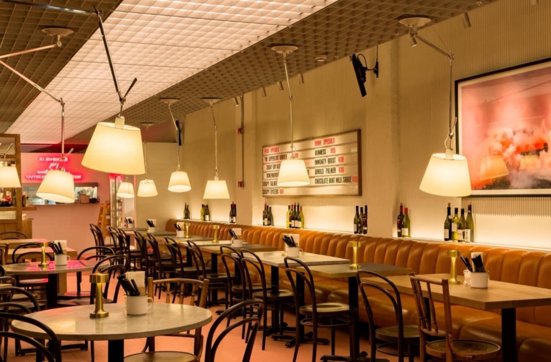 An interior view of a modern cafe with leather seating, round tables, and hanging lamps.