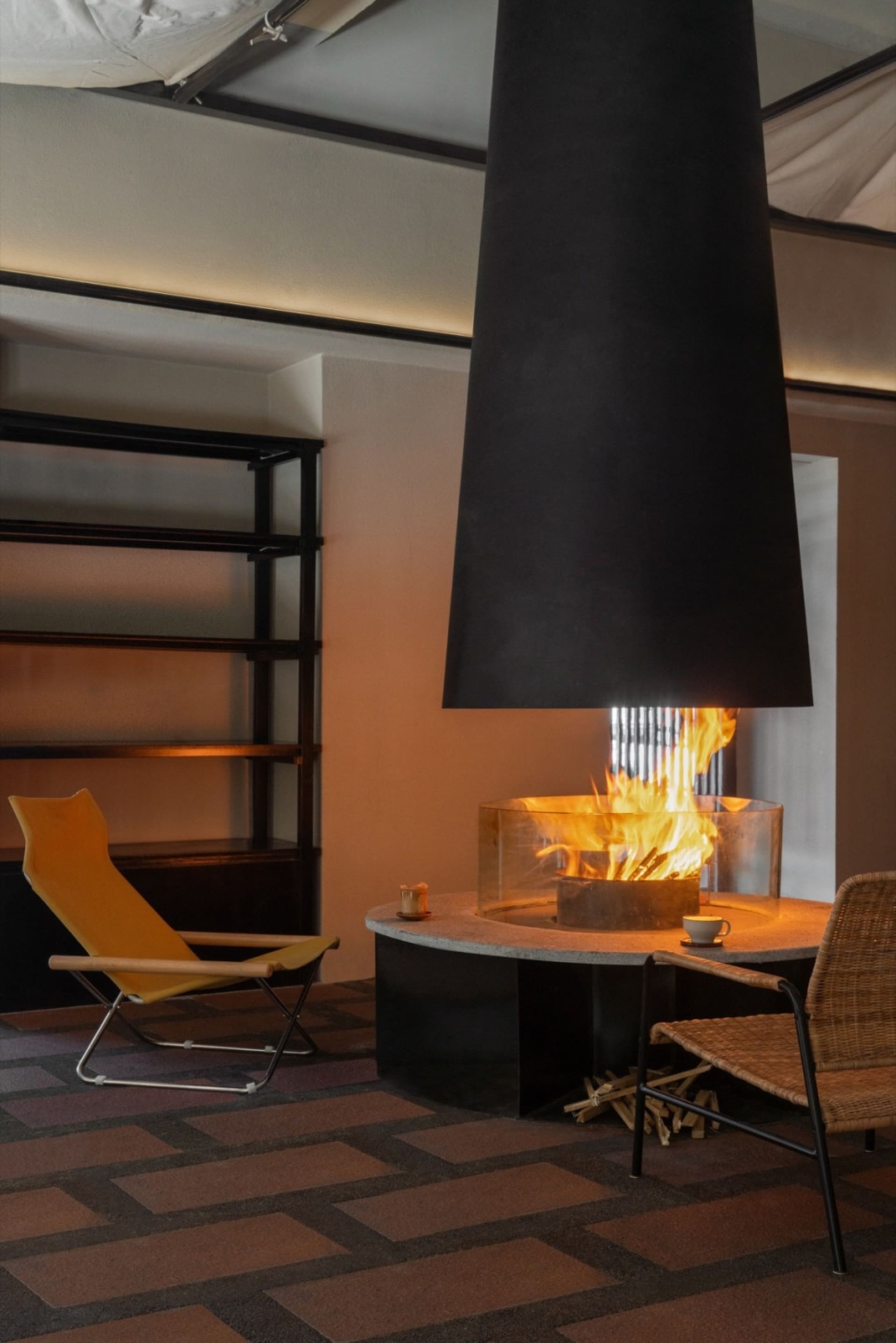 A modern lounge area featuring a steel fireplace and minimalist furniture.