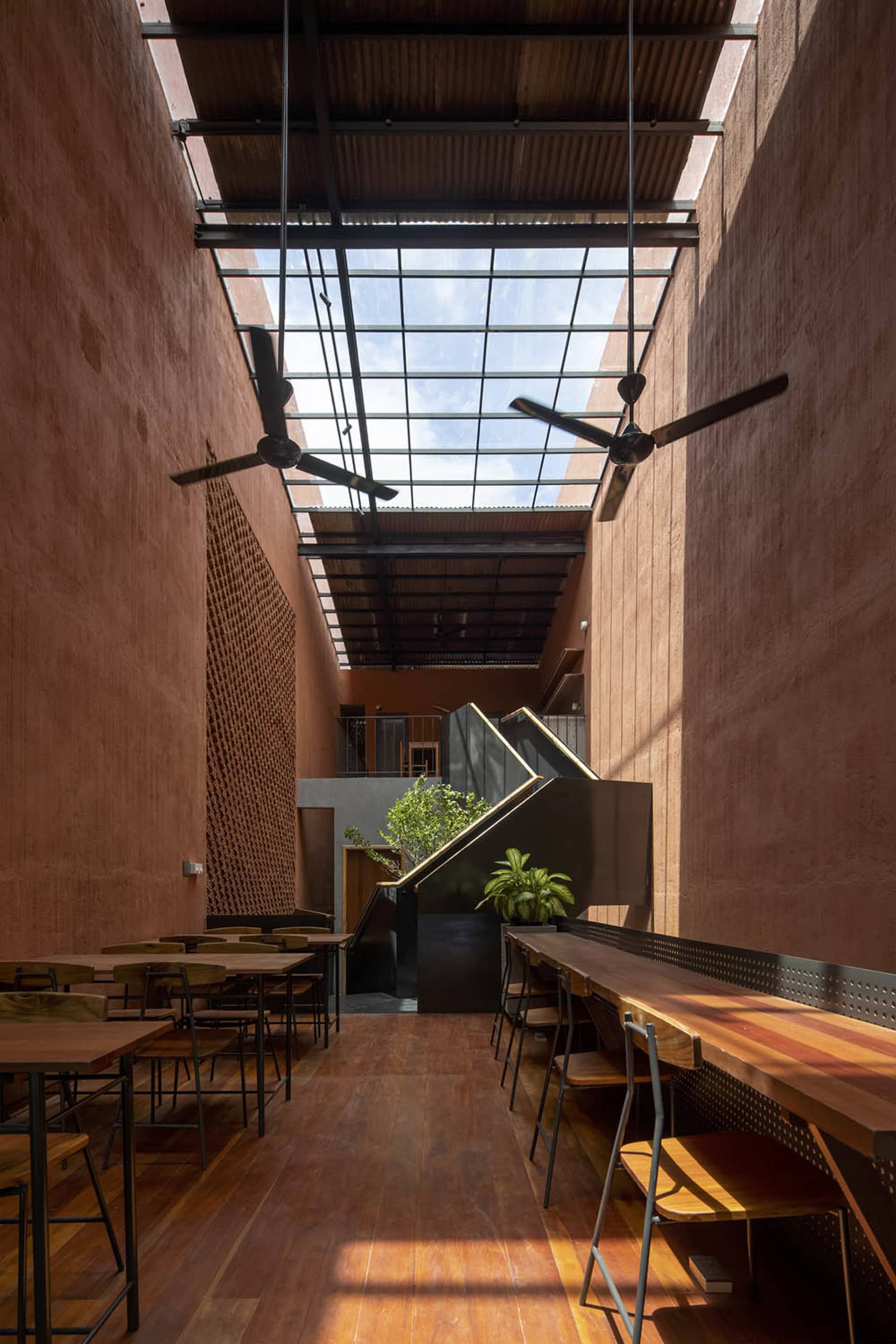 工業風餐廳室內,搭配木製餐桌與陶土色牆面,並設有玻璃天花板面板。