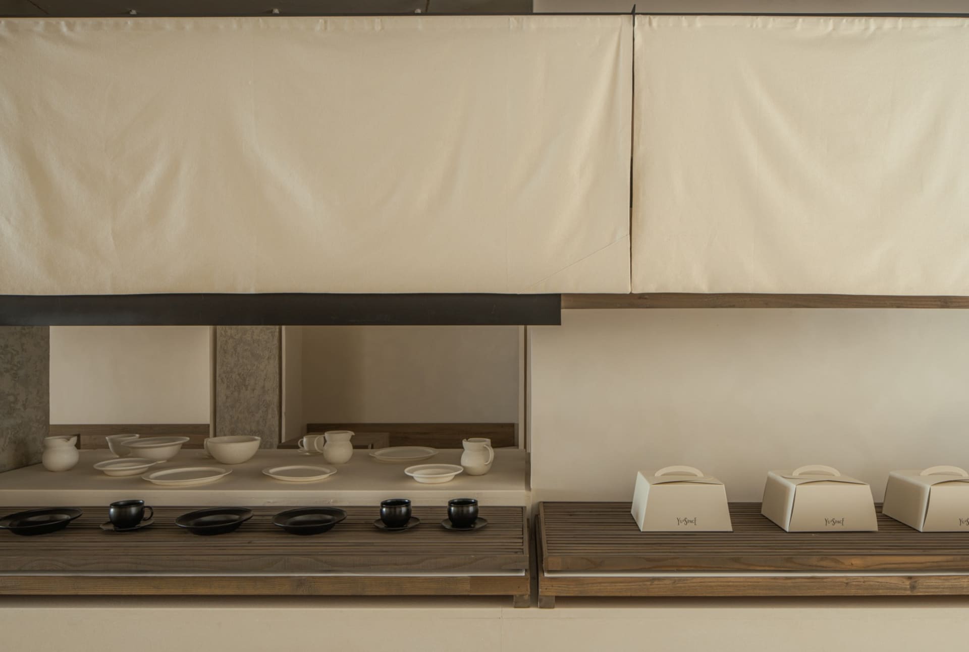 A modern coffee shop display featuring wooden shelves with white ceramic dishes and black coffee cups.