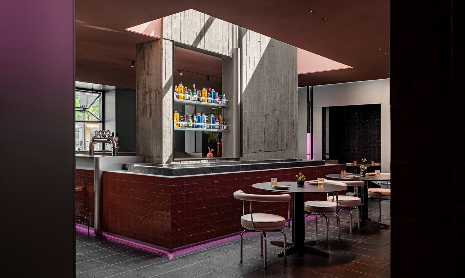 Modern cafe-bar interior with concrete walls and tables surrounded by chairs.