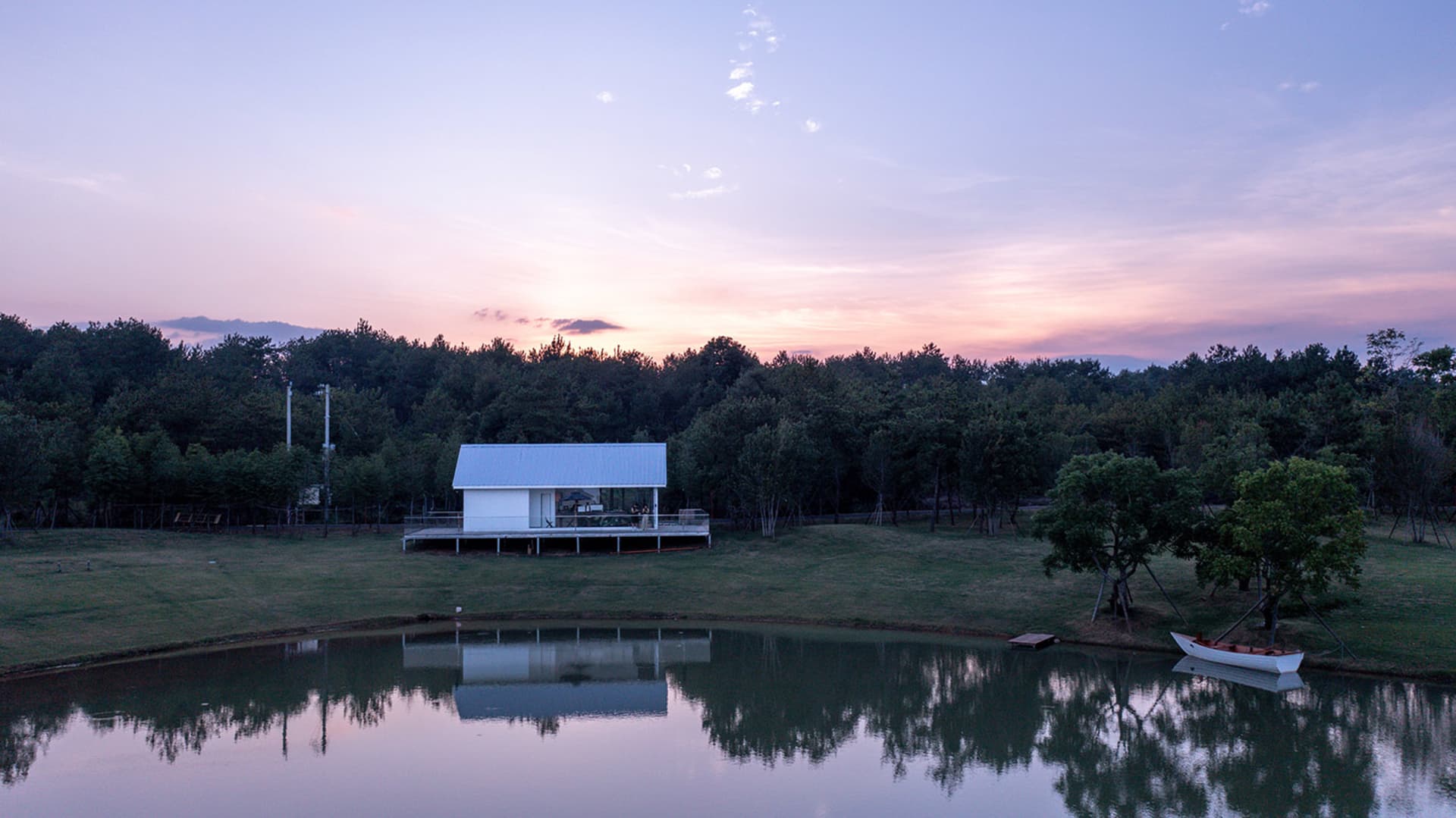 A tranquil scene featuring a white house on stilts overlooking a serene lake at sunset with trees in the background.