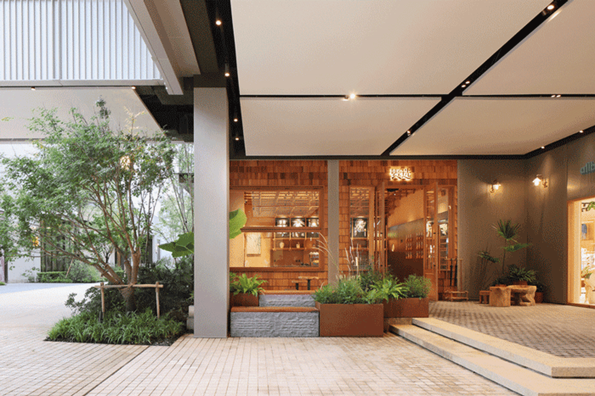 Concrete and wooden restaurant entrance with plants and a tree.