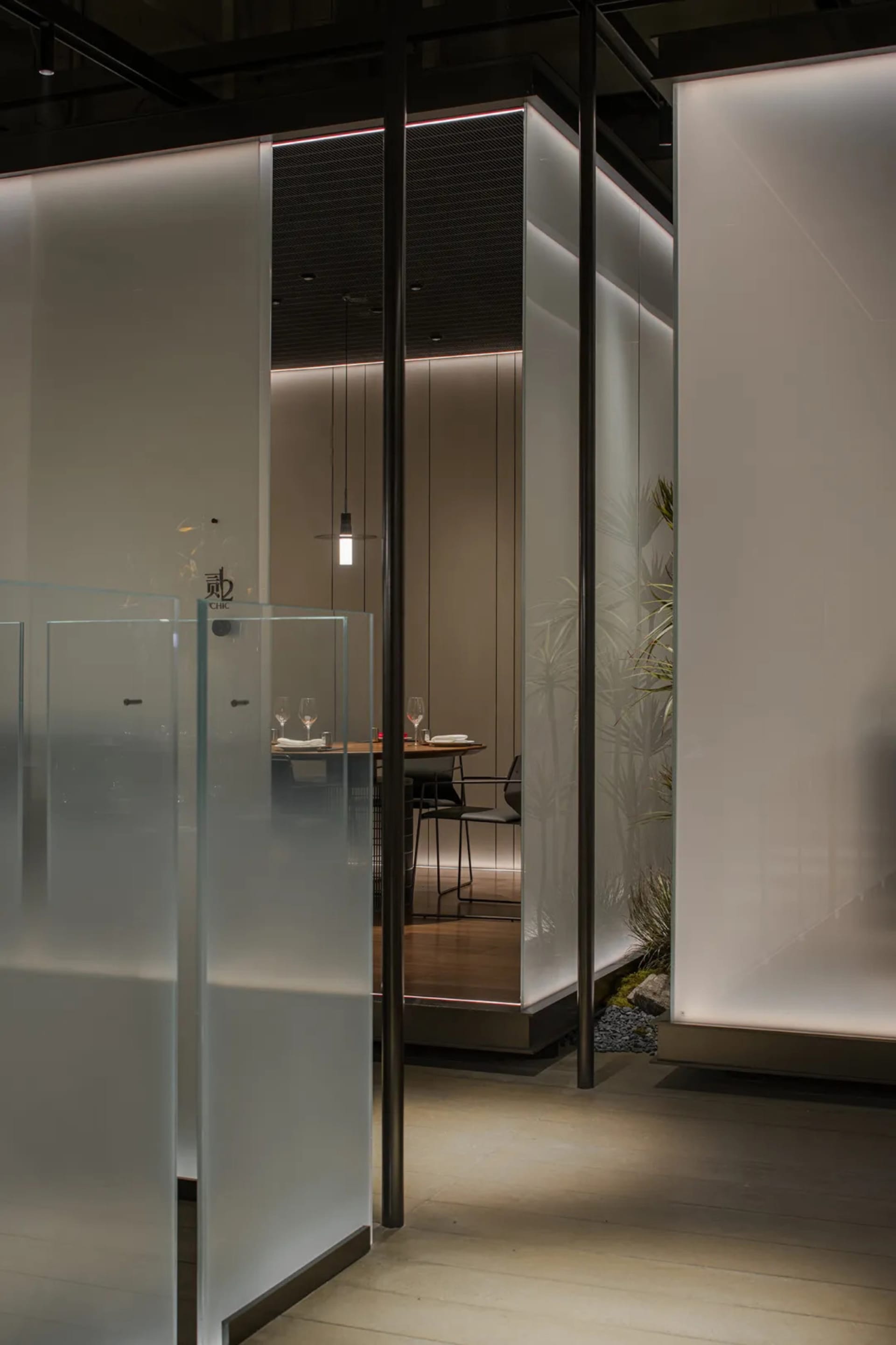 Modern restaurant private dining room with glass walls, wooden floor, and decorative plants.