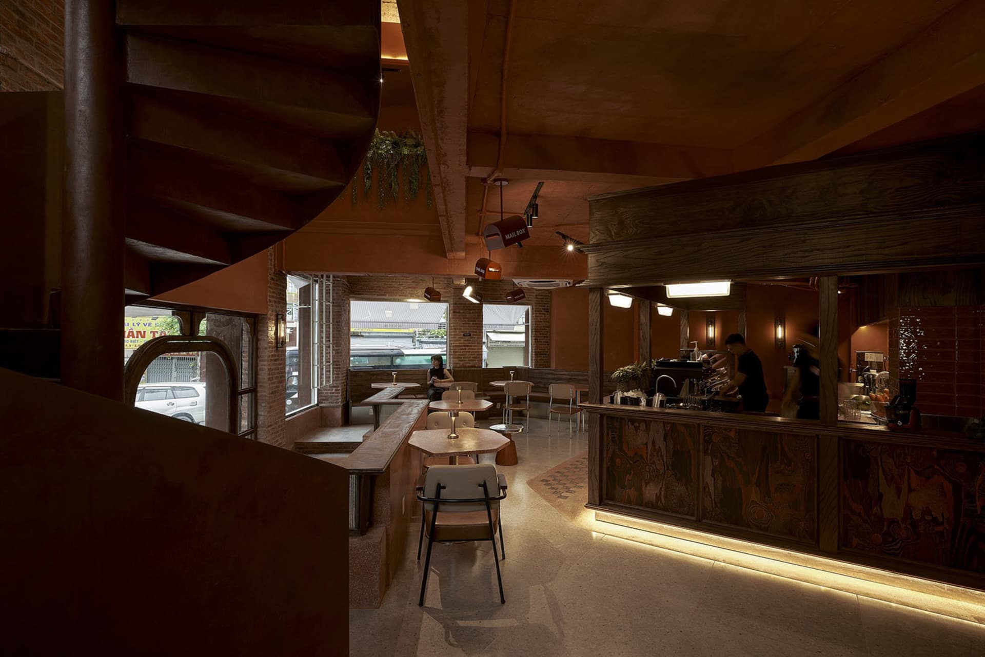 Industrially designed cafe interior featuring concrete and brick walls, wooden ceiling beams, and spiral staircase.