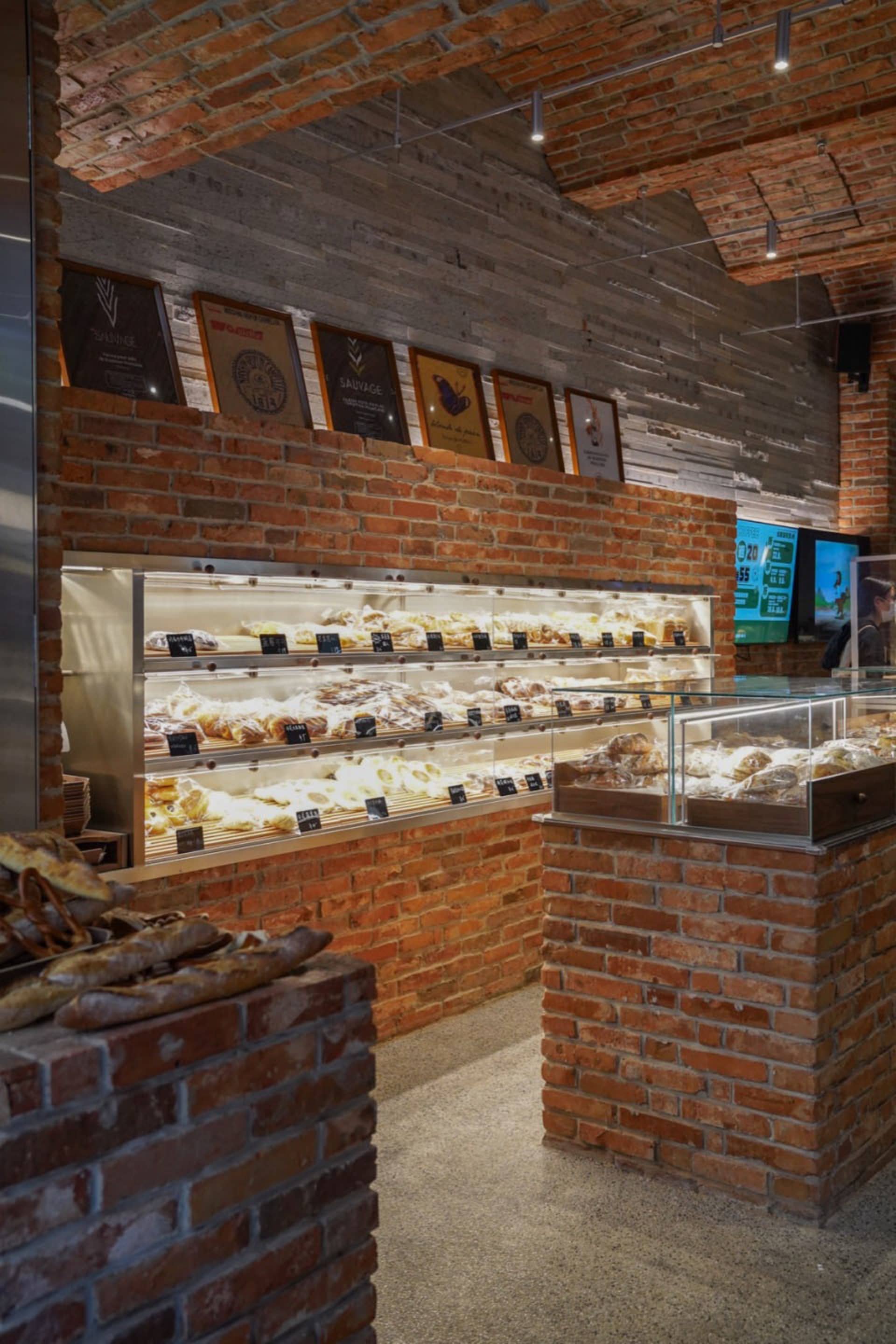 麵包店室內空間，裸露磚牆搭配展示櫃，櫃內陳列各式烘焙甜點。