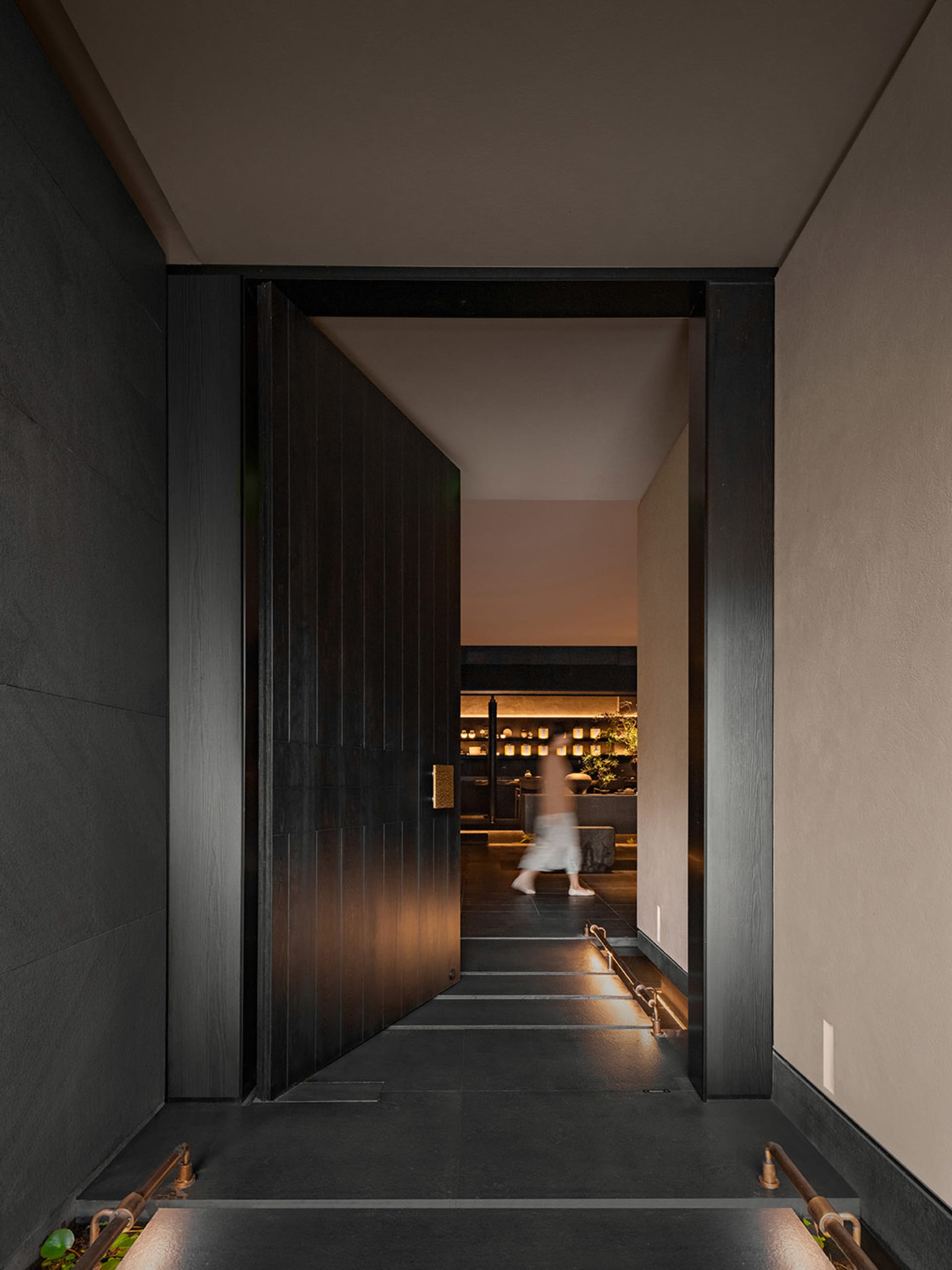 A modern minimalist entryway with a wooden door leading to a softly illuminated space.
