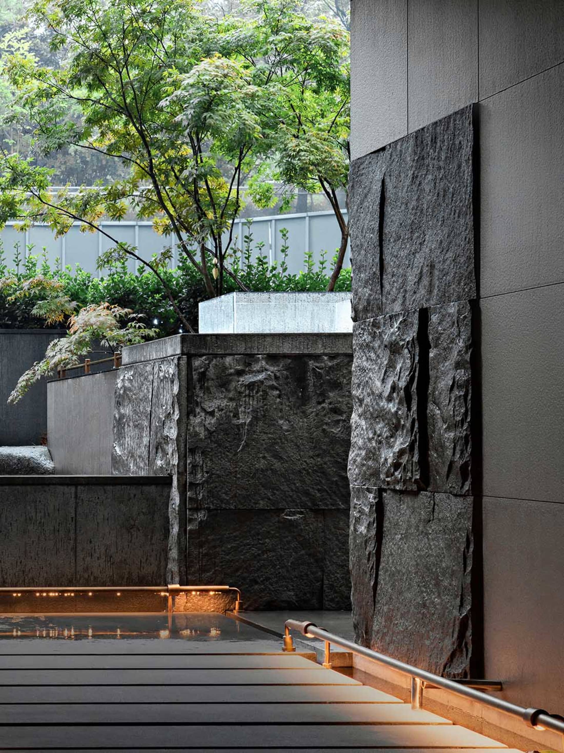 Urban water feature with black stone wall and greenery