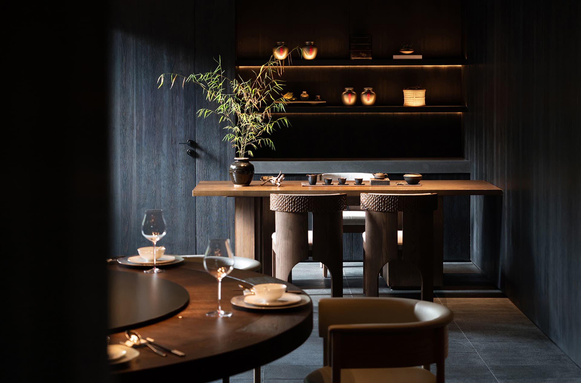 Modern restaurant interior with wooden tables, chairs, and dark, minimalist decor.