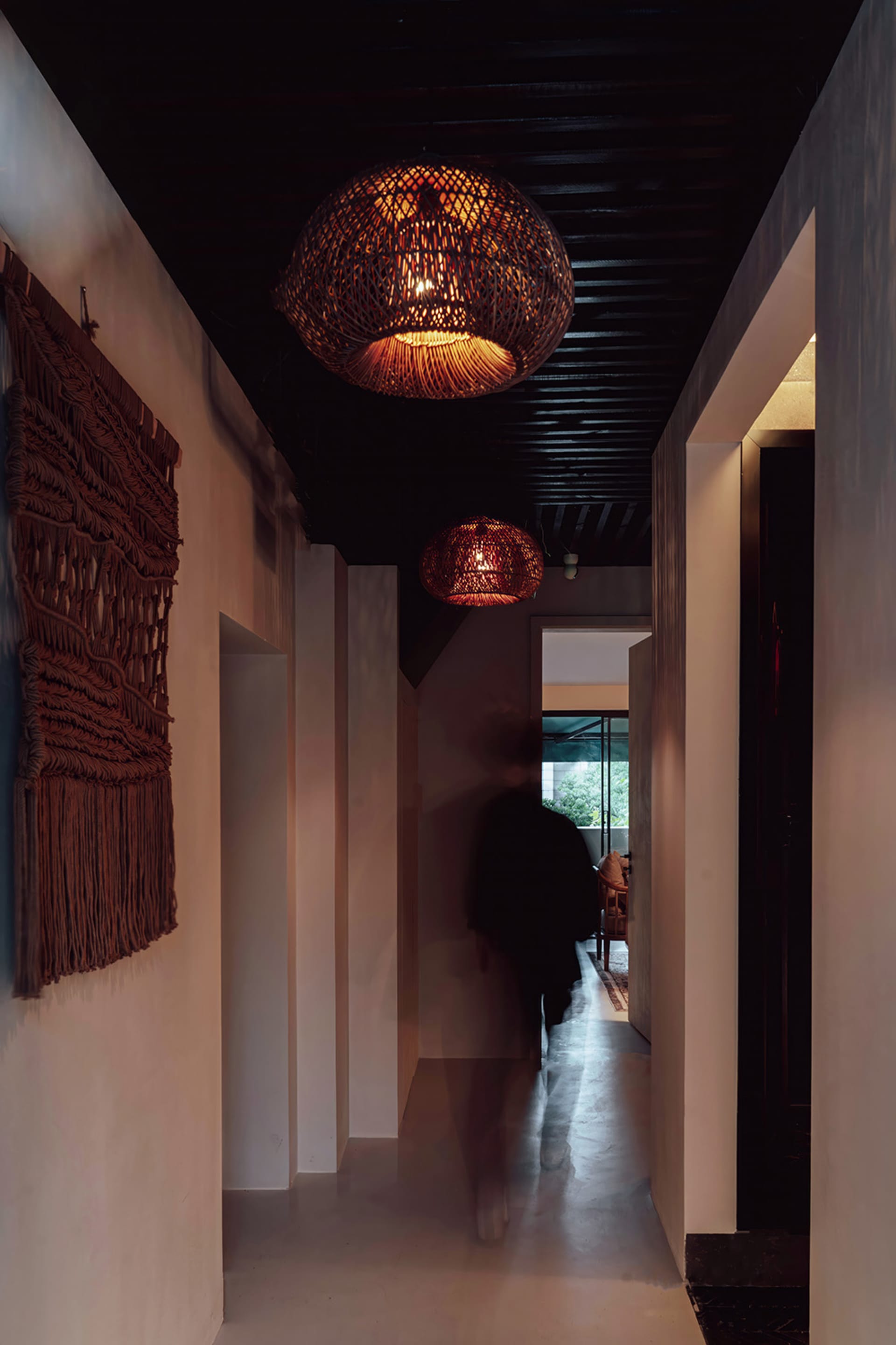 A minimalist hallway with woven rattan pendant lights hanging from a black wooden ceiling.