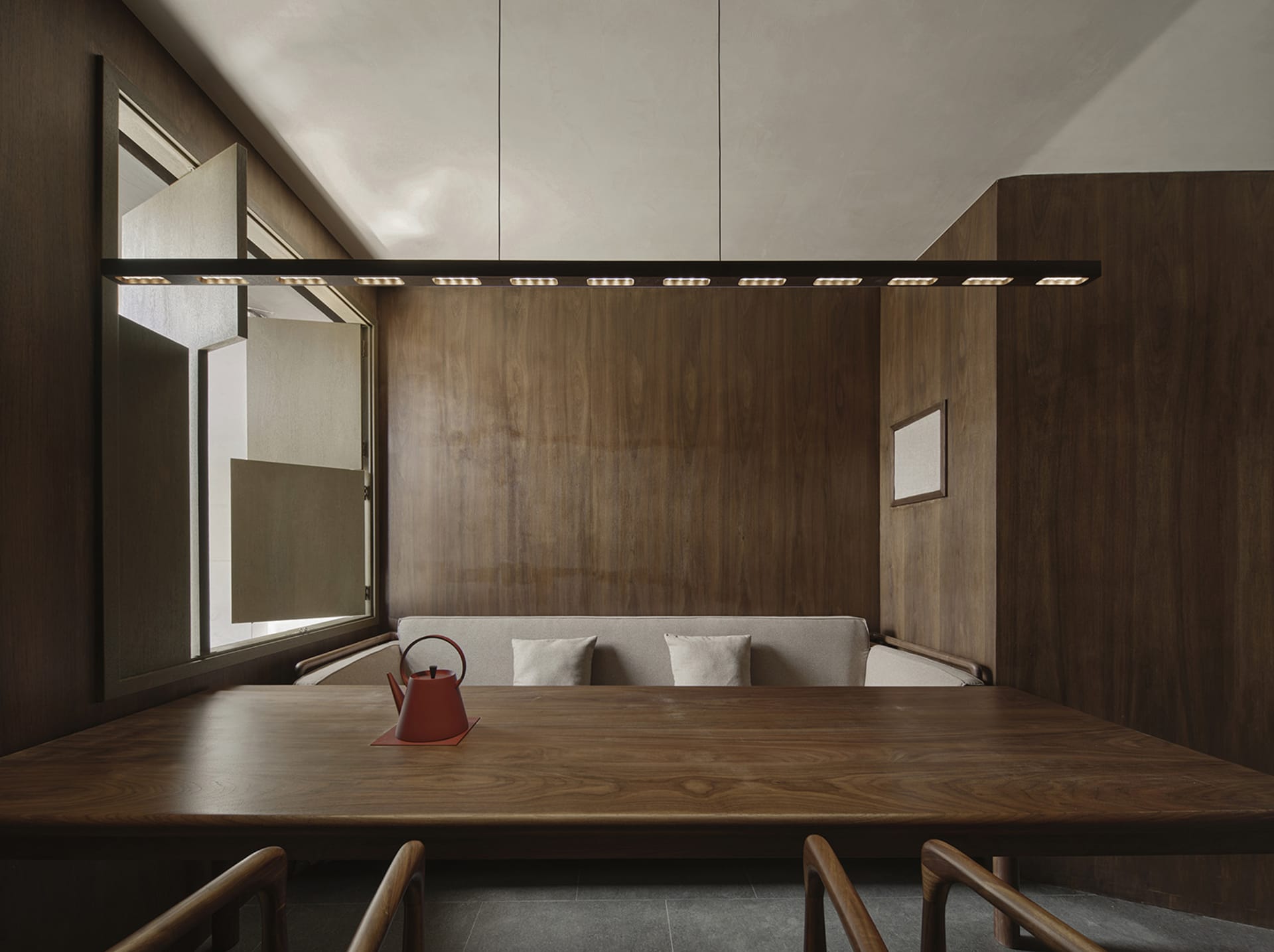 A minimalist interior with wooden walls and a wooden table, featuring a red teapot as a centerpiece.