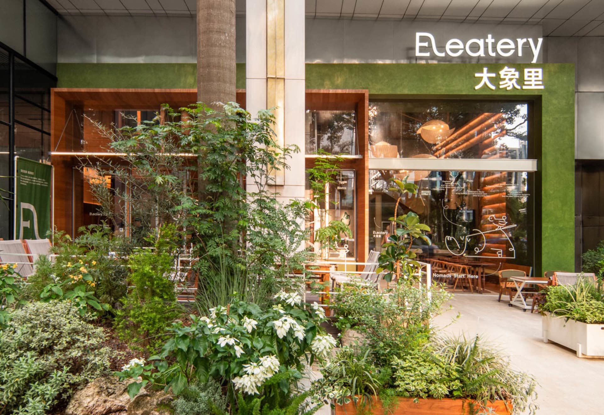 A modern casual cafe with green interiors, made from wood, stone, and glass, featuring a central table and chairs.