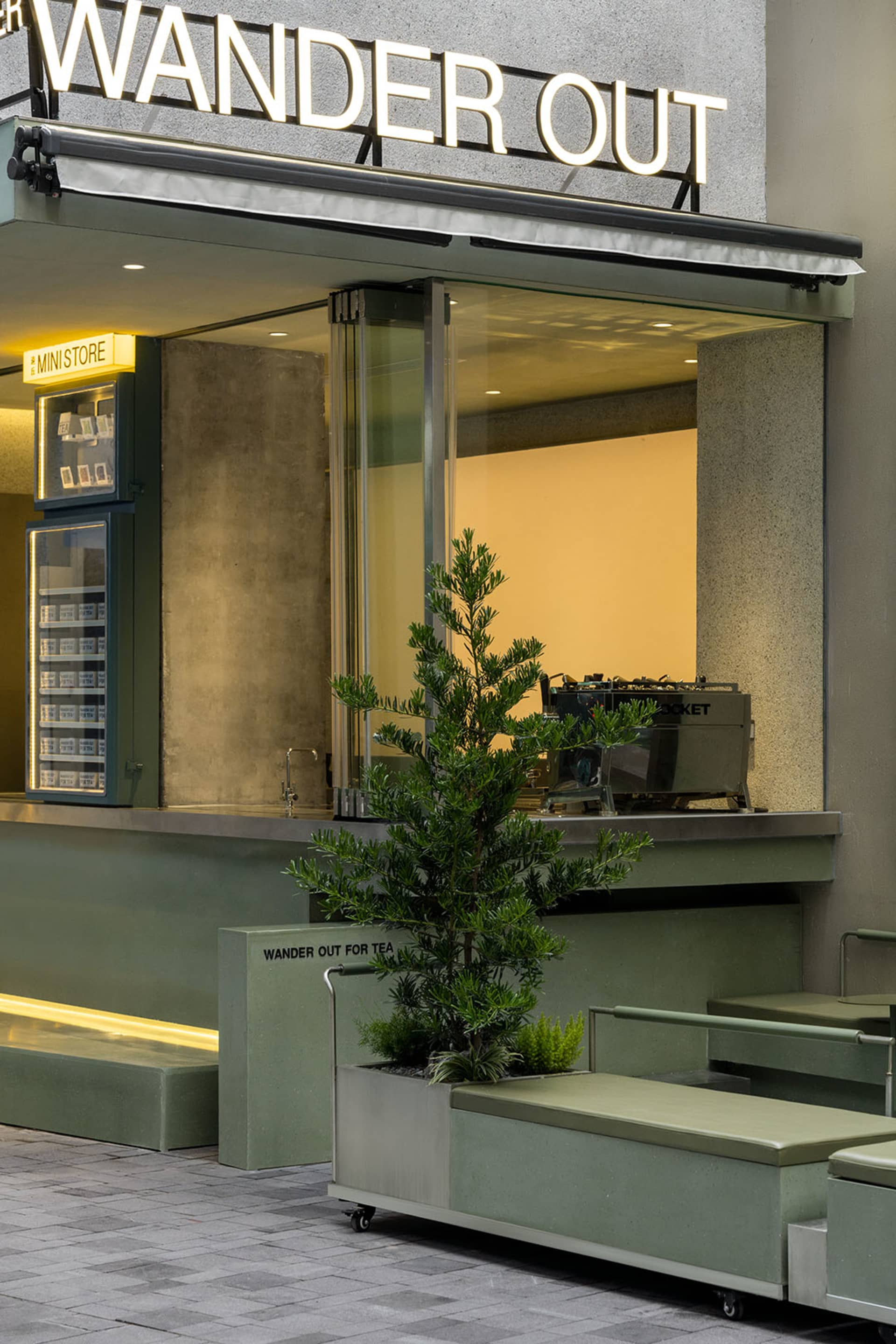 Industrial-style cafe storefront with concrete walkway, glass windows, and potted plants.