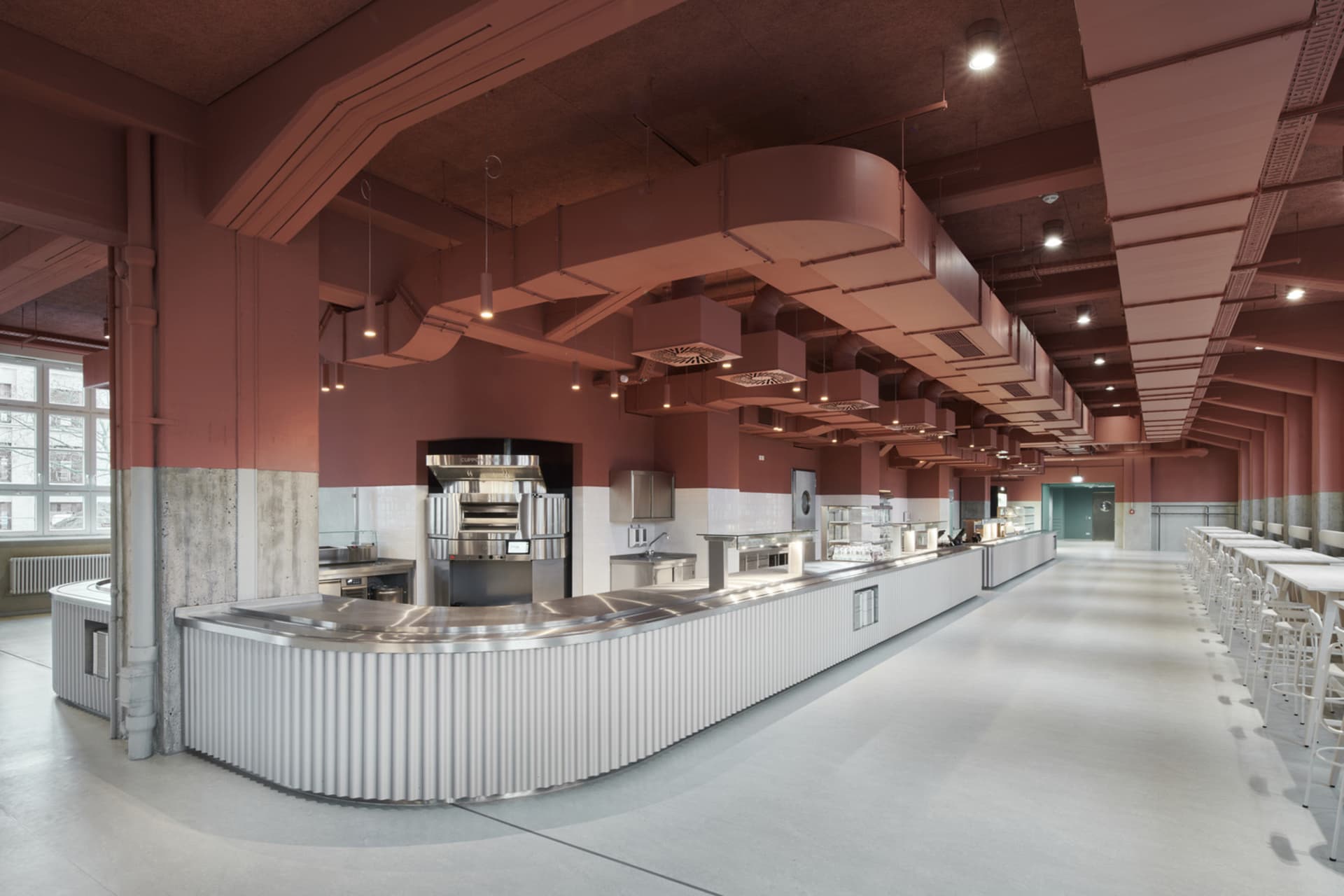 工業風自助餐廳,設有長條金屬餐台、白瓷磚背牆,以及裸露的通風管線。