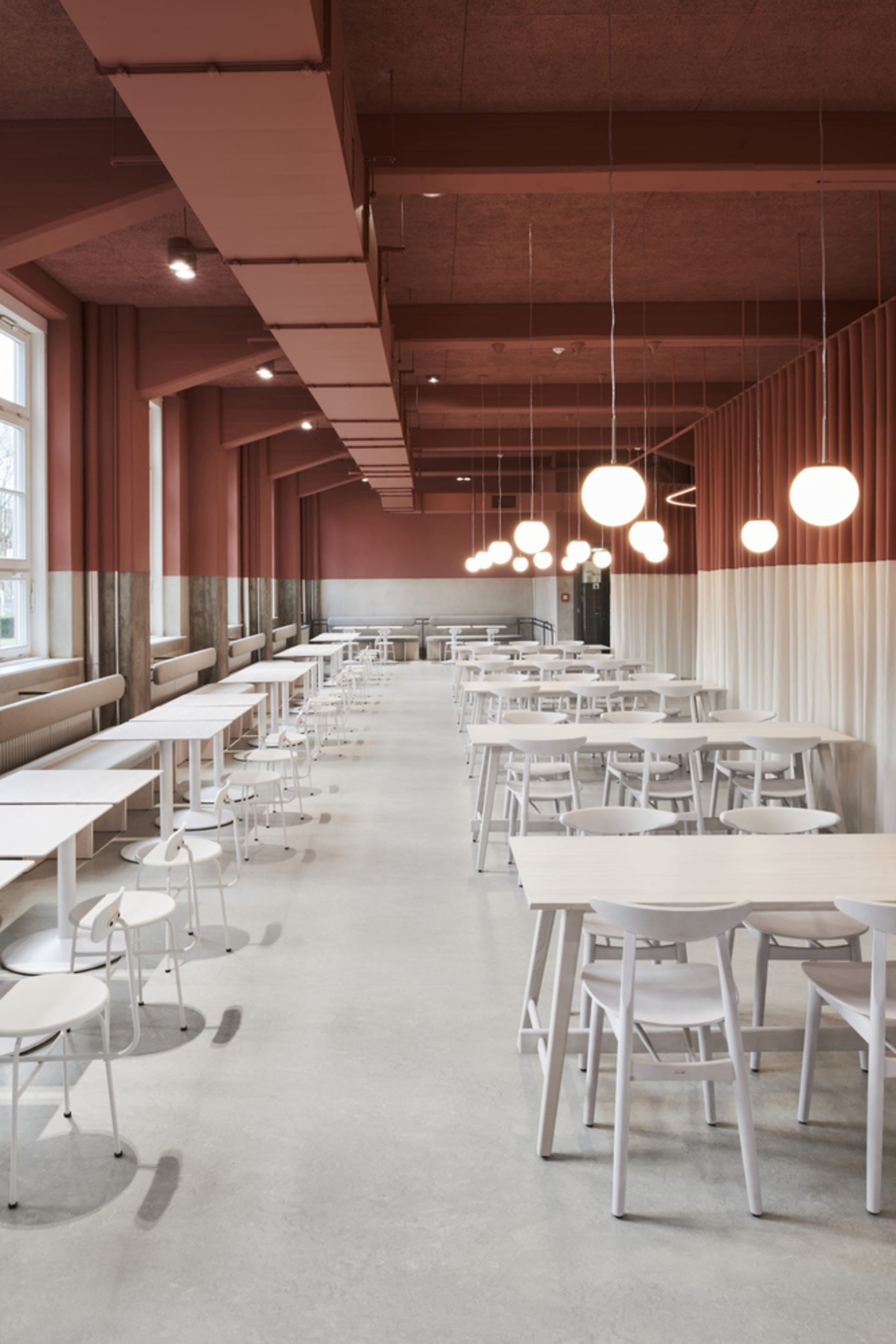 A spacious, modern cafeteria with multiple white tables and chairs arranged neatly in rows. The ceiling is painted in a warm