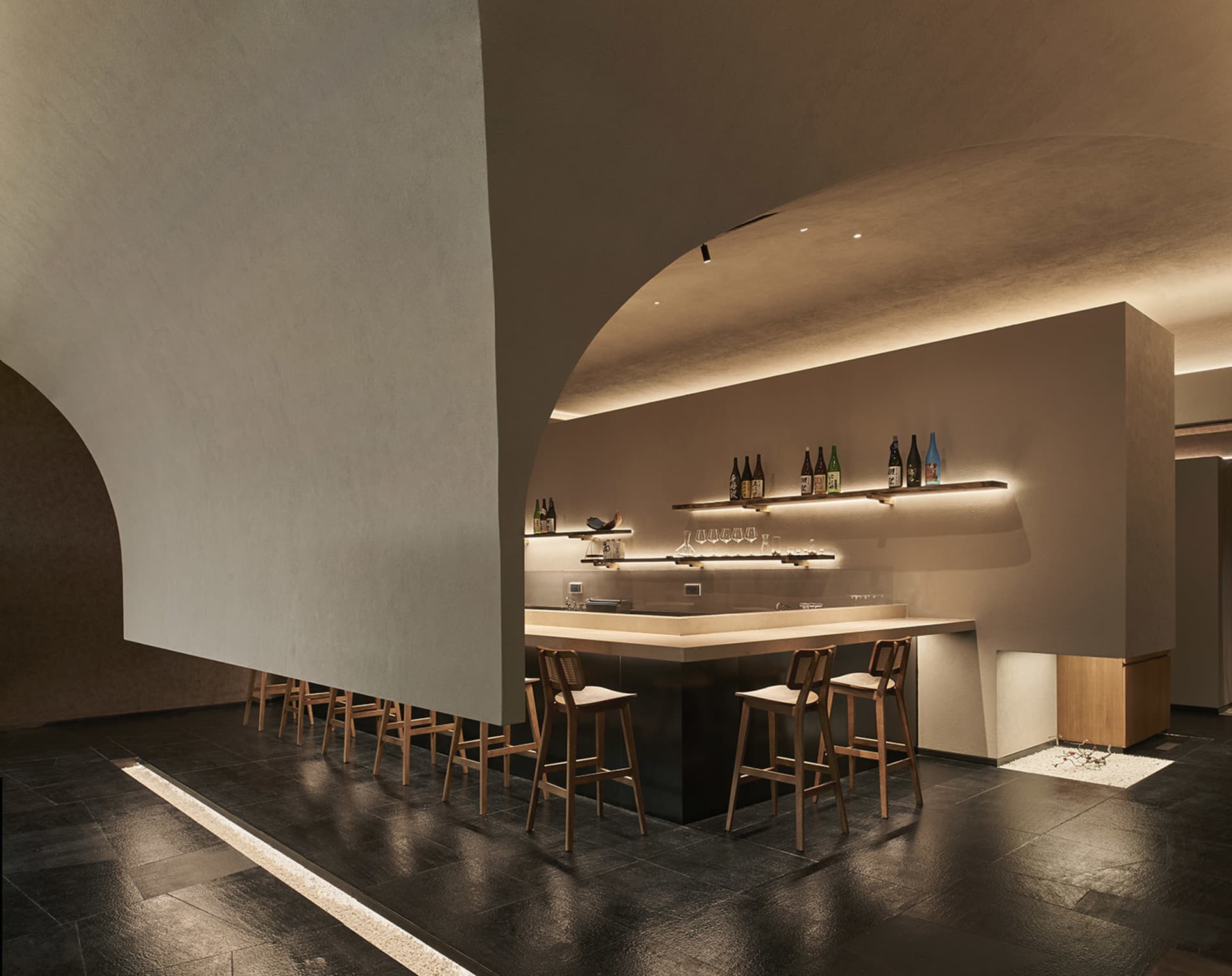 Modern, minimalist bar with concrete walls and wooden barstools, featuring a warm, inviting atmosphere.
