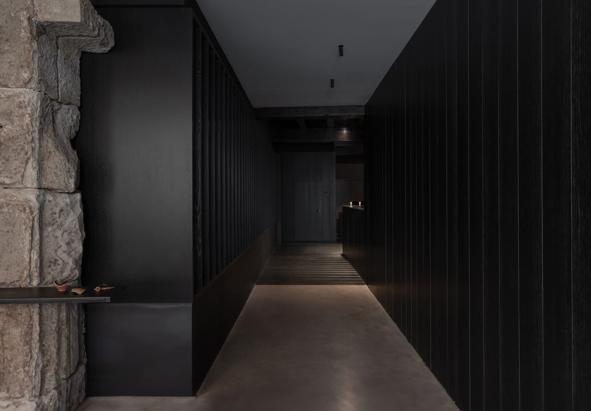 A minimalist corridor interior with stone walls and concrete flooring.