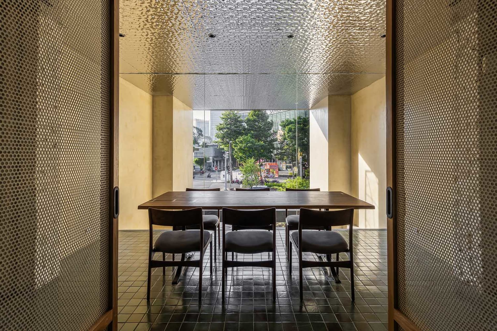 A modern dining room with a wooden table and chairs in front of a large window showing an urban street view.