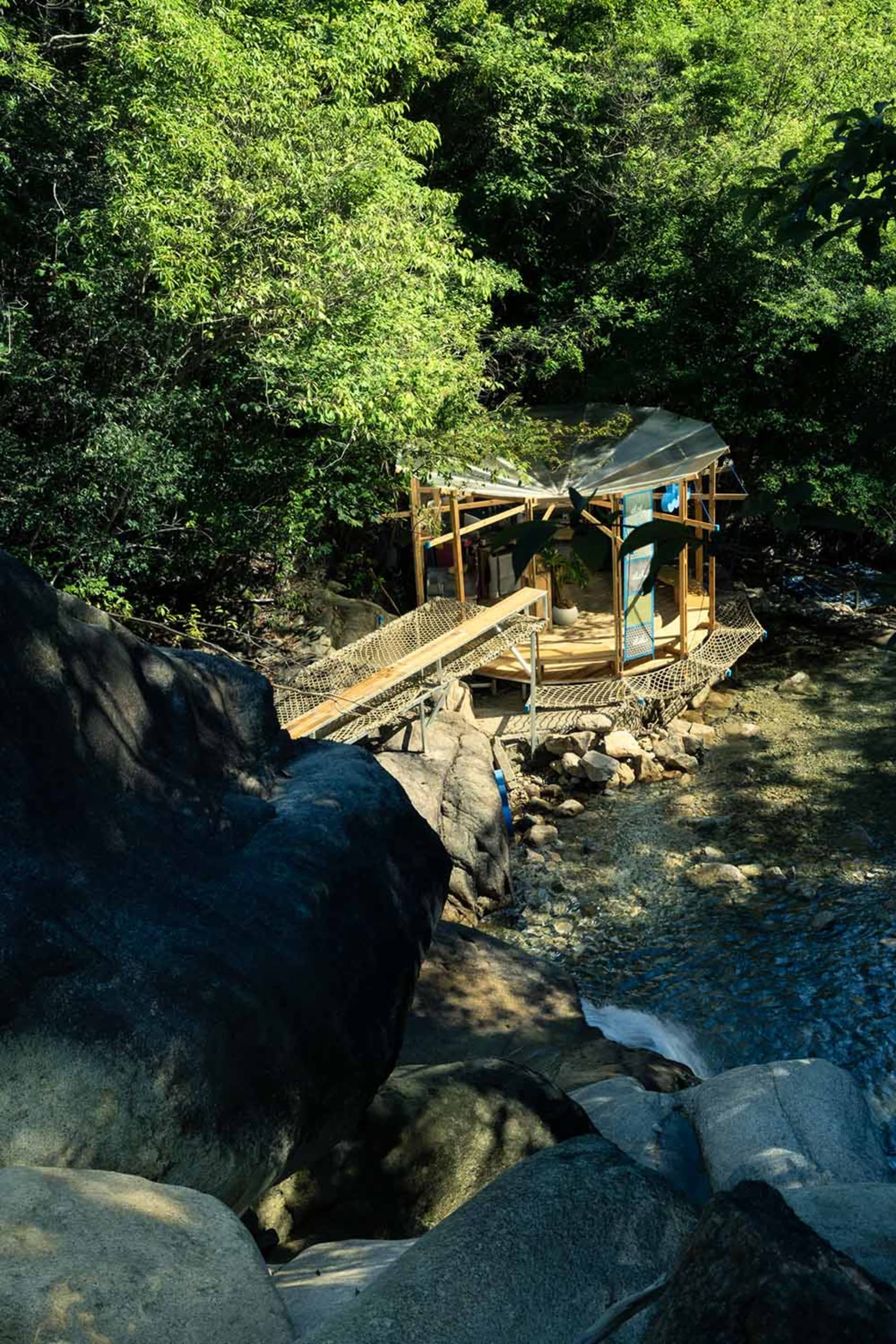 A wooden and netted structure built along a rocky stream in a forest.