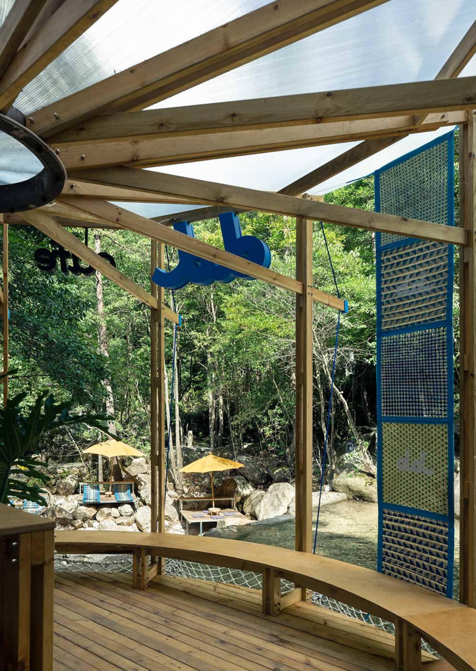 A wooden gazebo with a glass roof provides an outdoor restaurant seating area surrounded by nature.