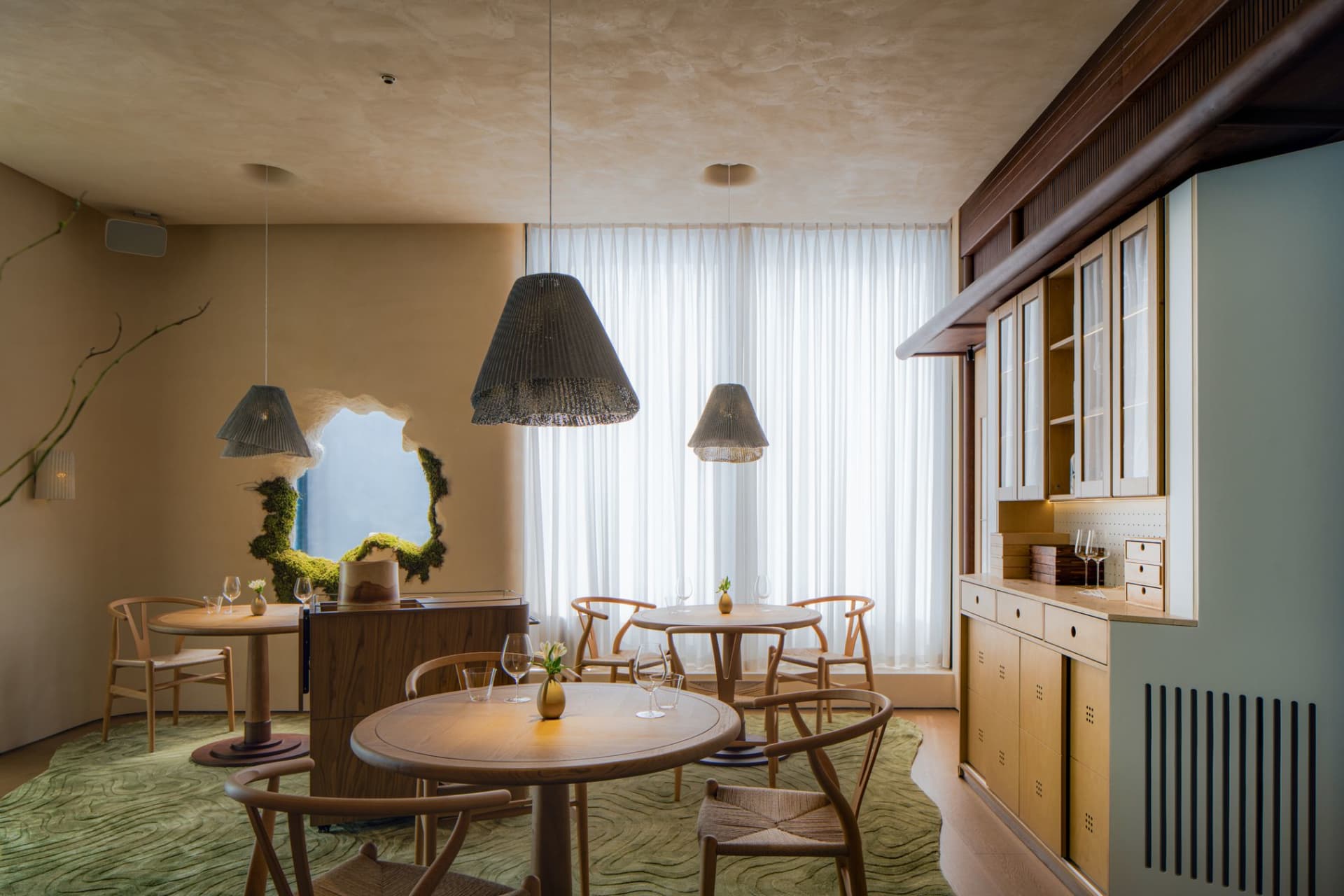 Modern restaurant interior with wooden tables, fabric curtains, and a window showcasing the outdoors.
