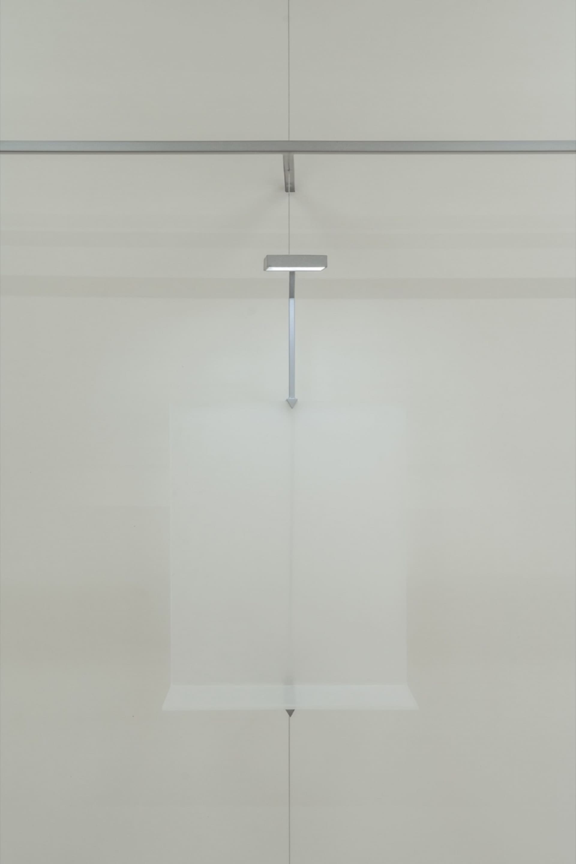 A minimalist glass floating object installation art piece mounted on a white wall.