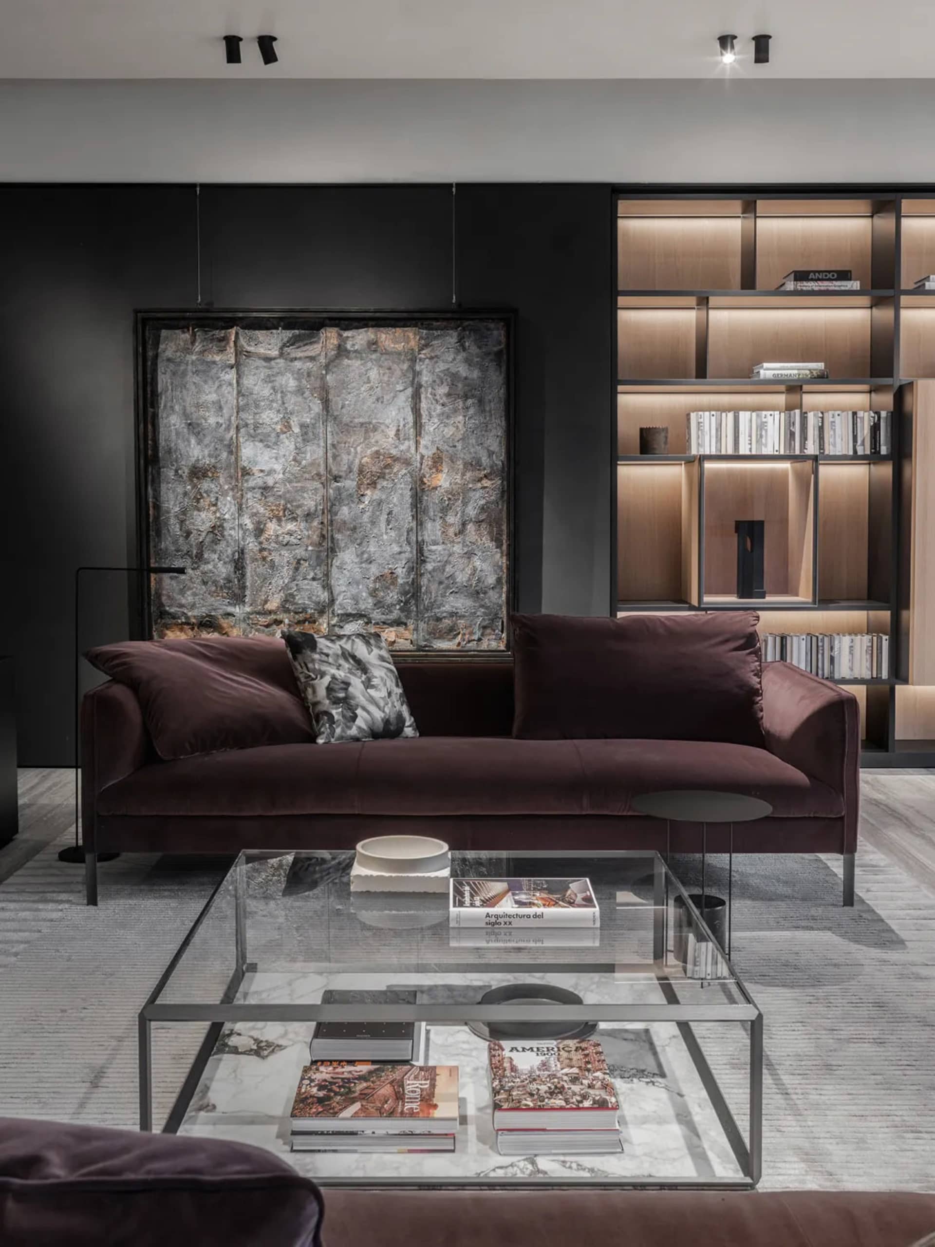 Modern living room with a purple velvet couch, glass coffee table, and light wood shelves.