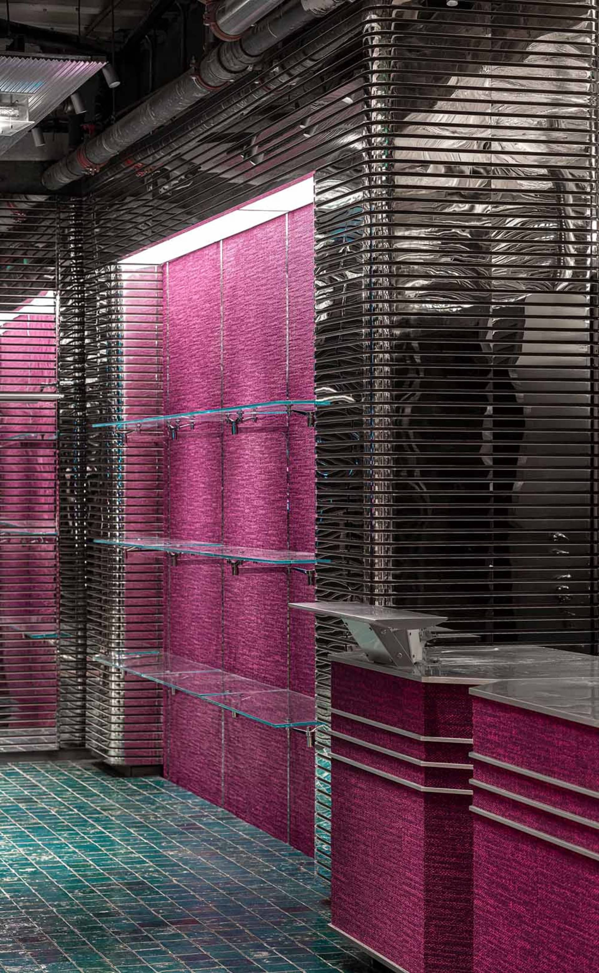 Modern retail space with metallic texture backdrop, glass shelves, and pink textile elements