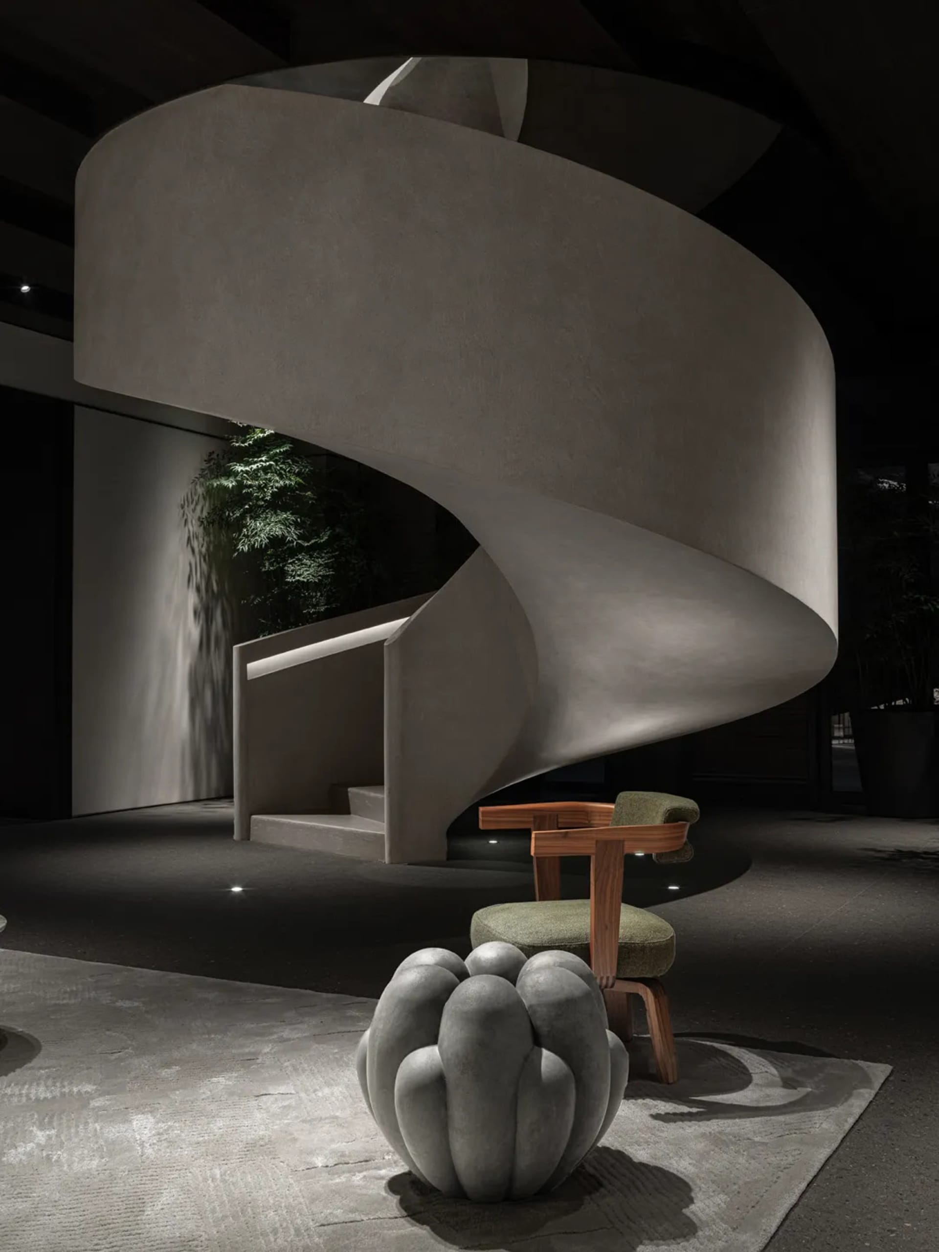 Modern, minimalist, concrete spiral staircase interior design with greenery and seating.