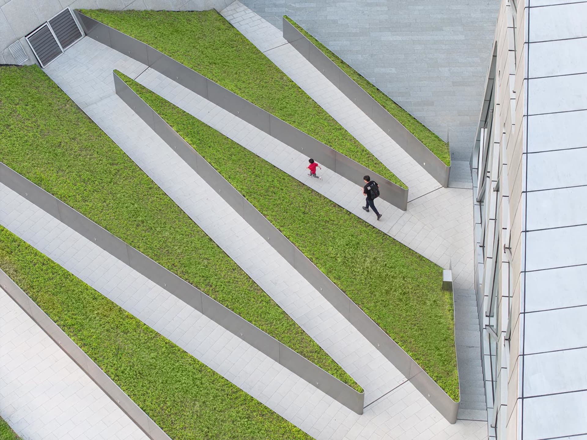 A modern urban green space featuring a green roof with concrete pathways and green grass bordered by metal frames.