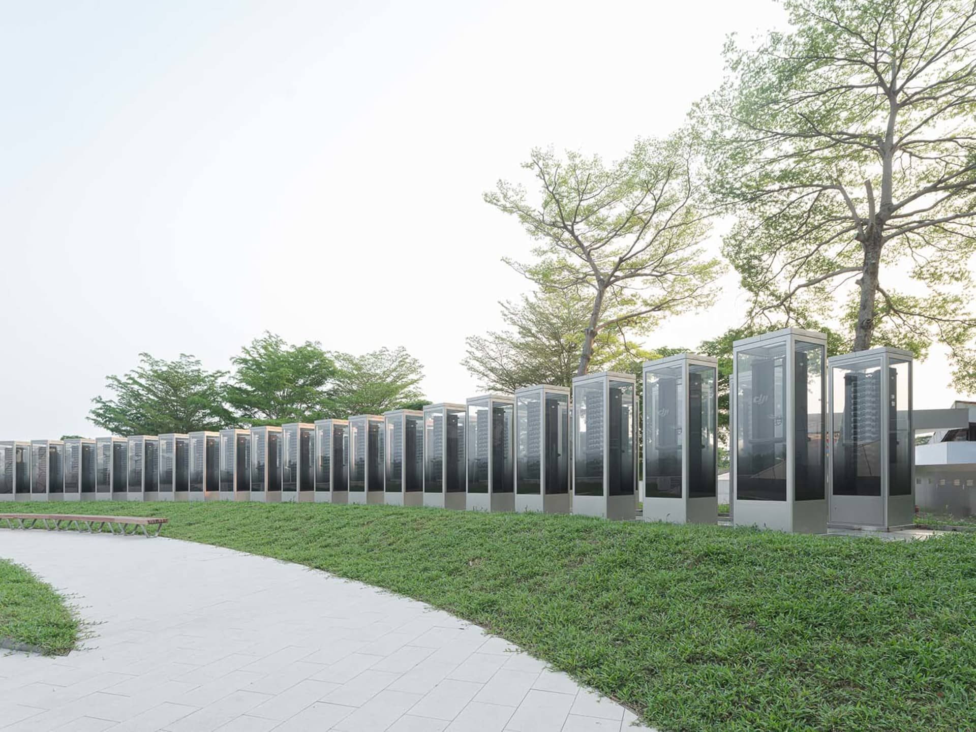 Rows of modern glass and steel structures in a park setting with greenery and trees.