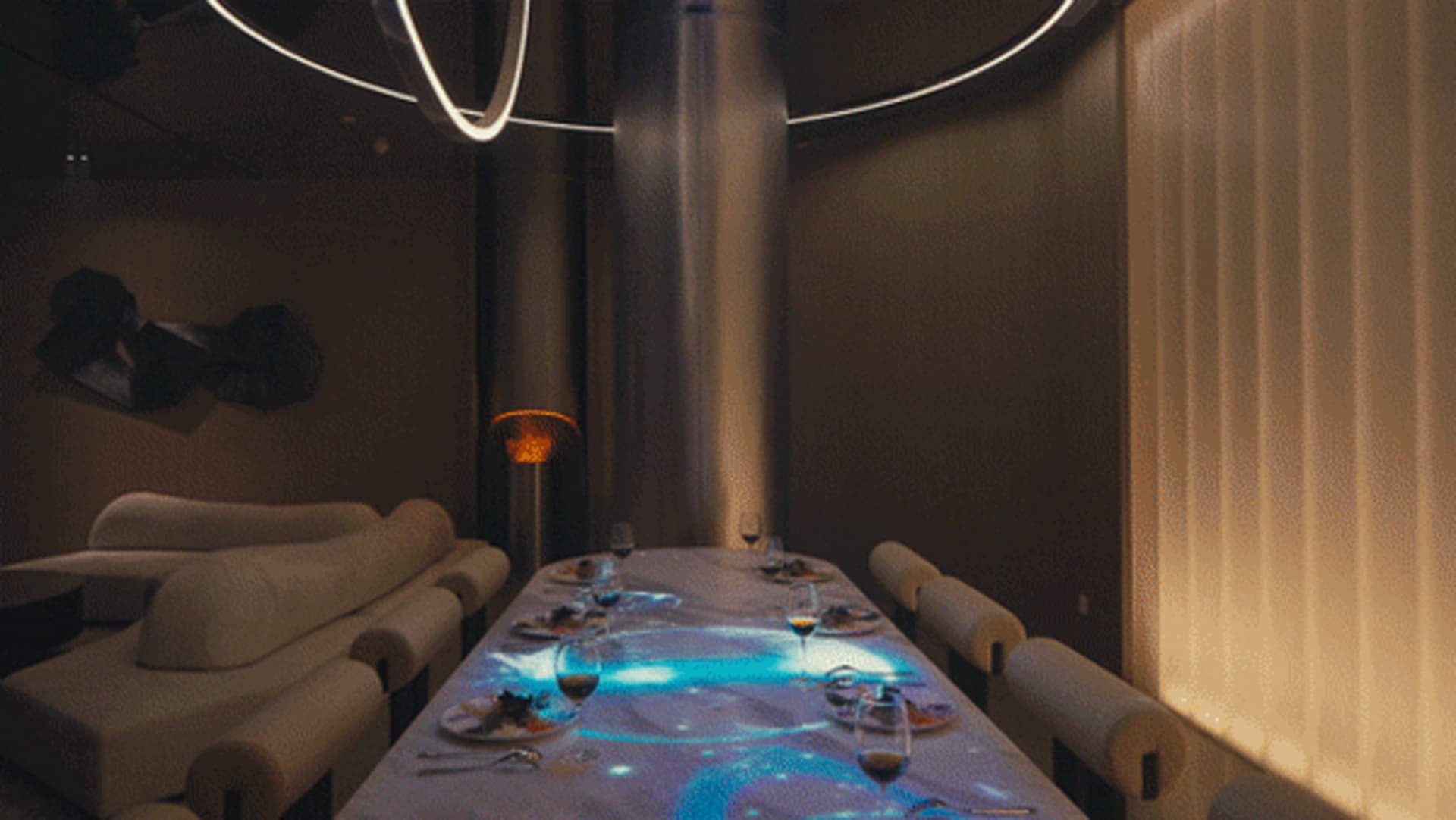 An empty industrial-style restaurant with a long dining table set for a meal and dim lighting.