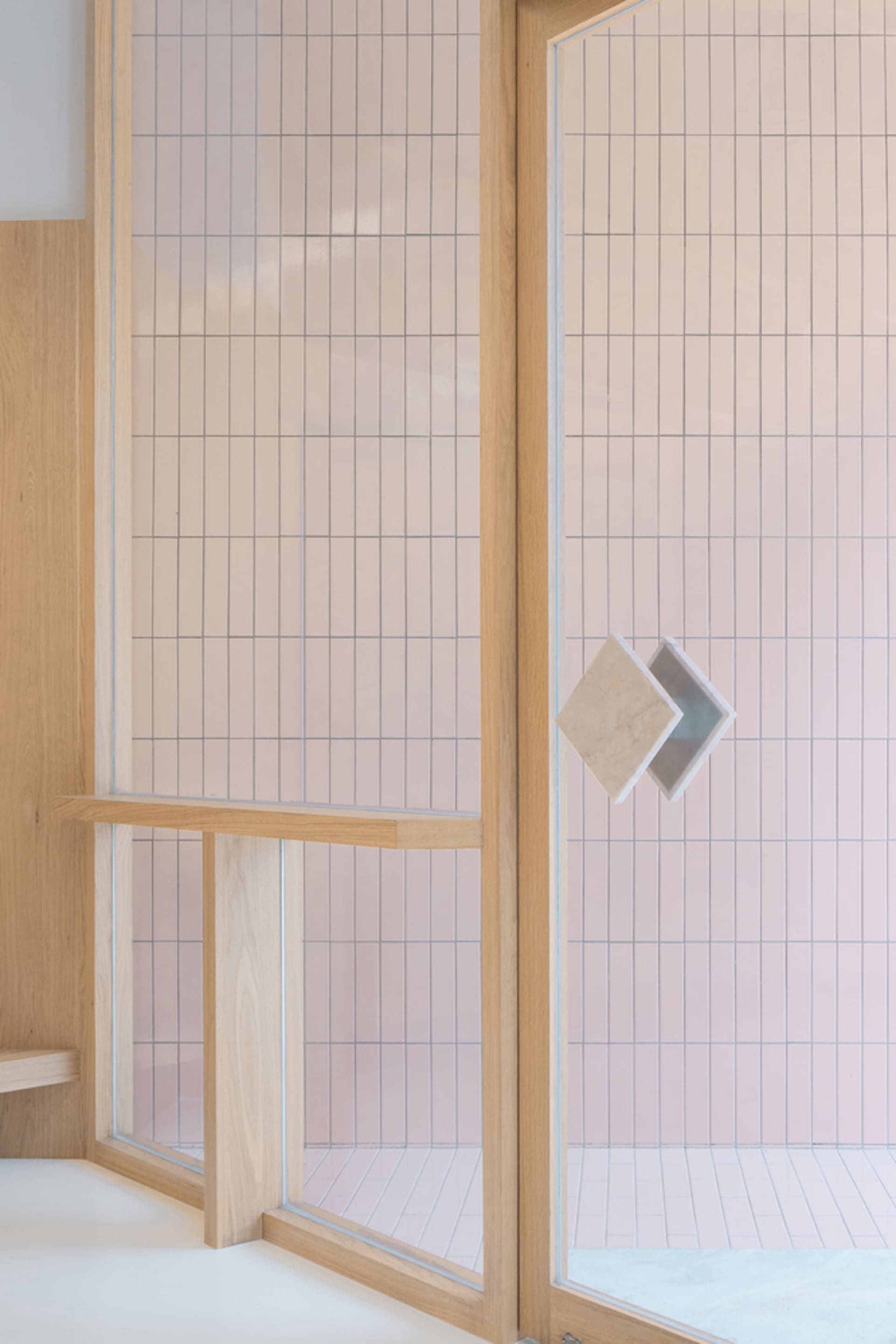 Modern minimalist bathroom with light pink square tiles on the walls and floor, framed by wooden accents.