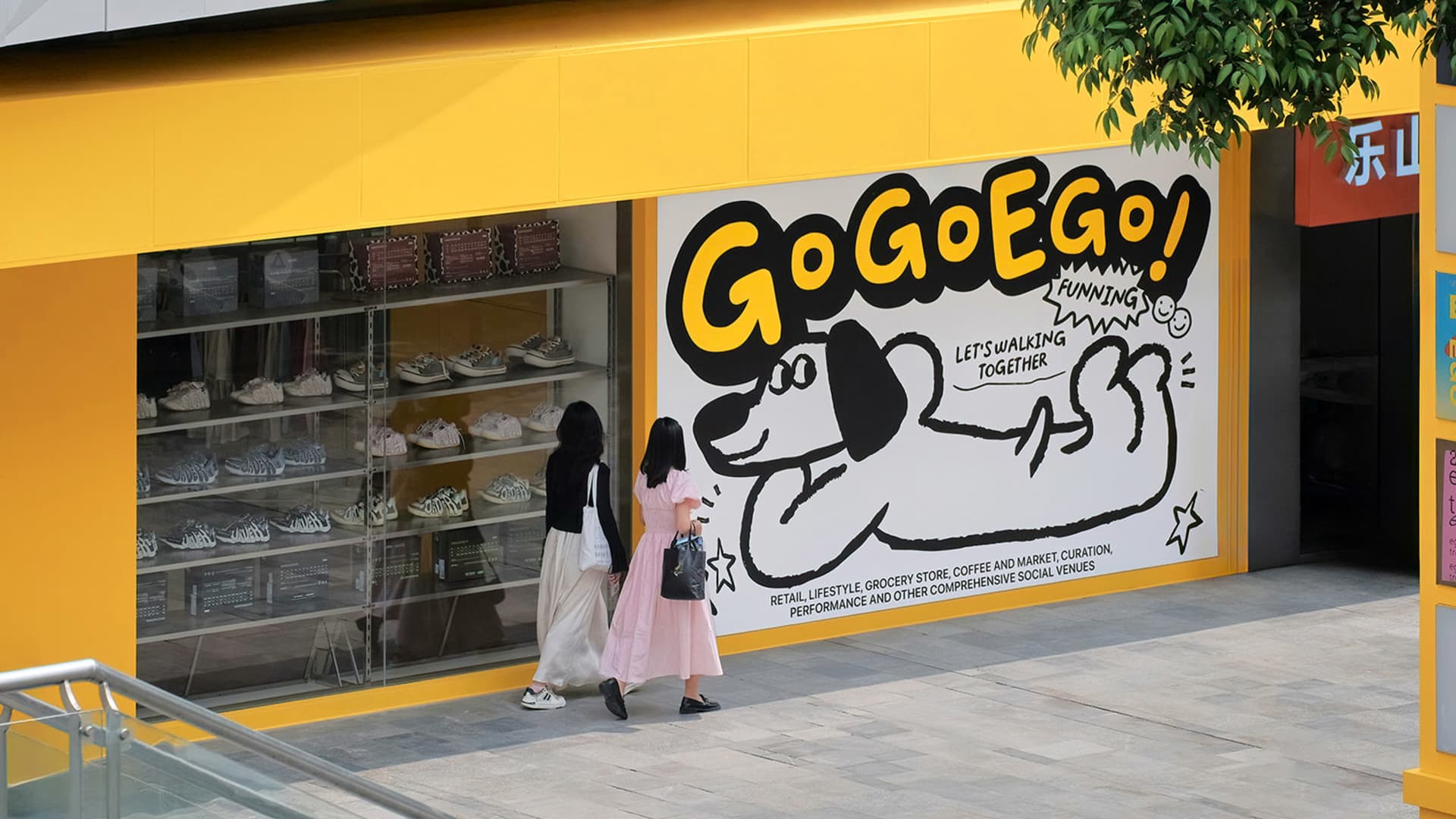 People walking past a storefront with a glass window display and a large mural featuring a cartoon dog.