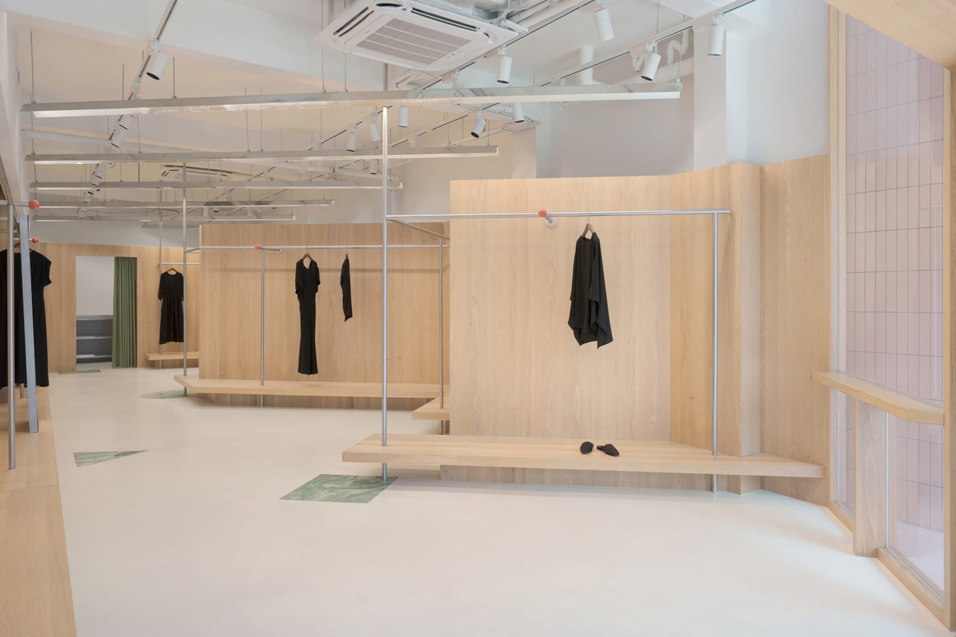 Modern minimalist retail display space featuring wooden and metal surfaces and concrete flooring, with clothing racks and sto