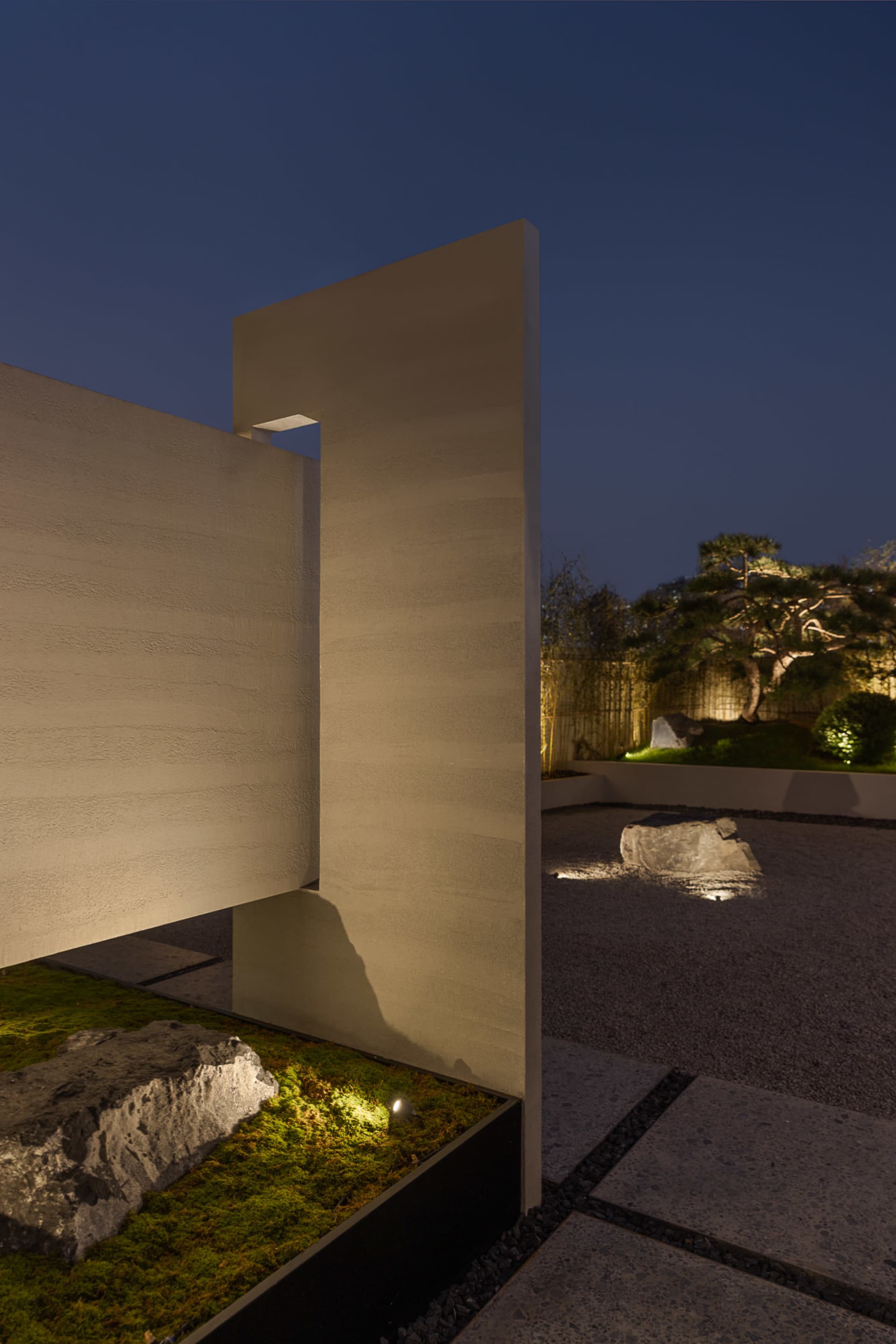 A minimalist residential courtyard featuring concrete surfaces, stone elements, and strategically placed lighting.