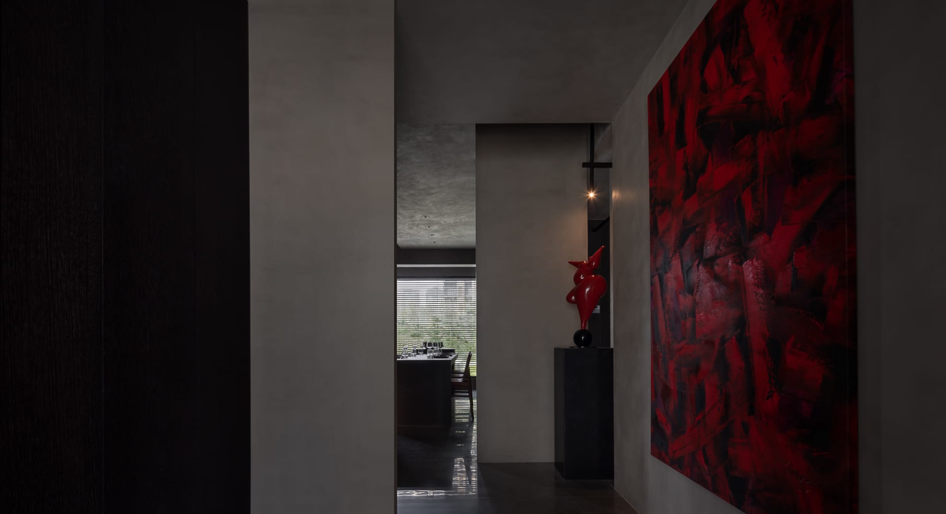 A modern dining room with a concrete minimalist design featuring a bright red artwork and a red sculptural vase.