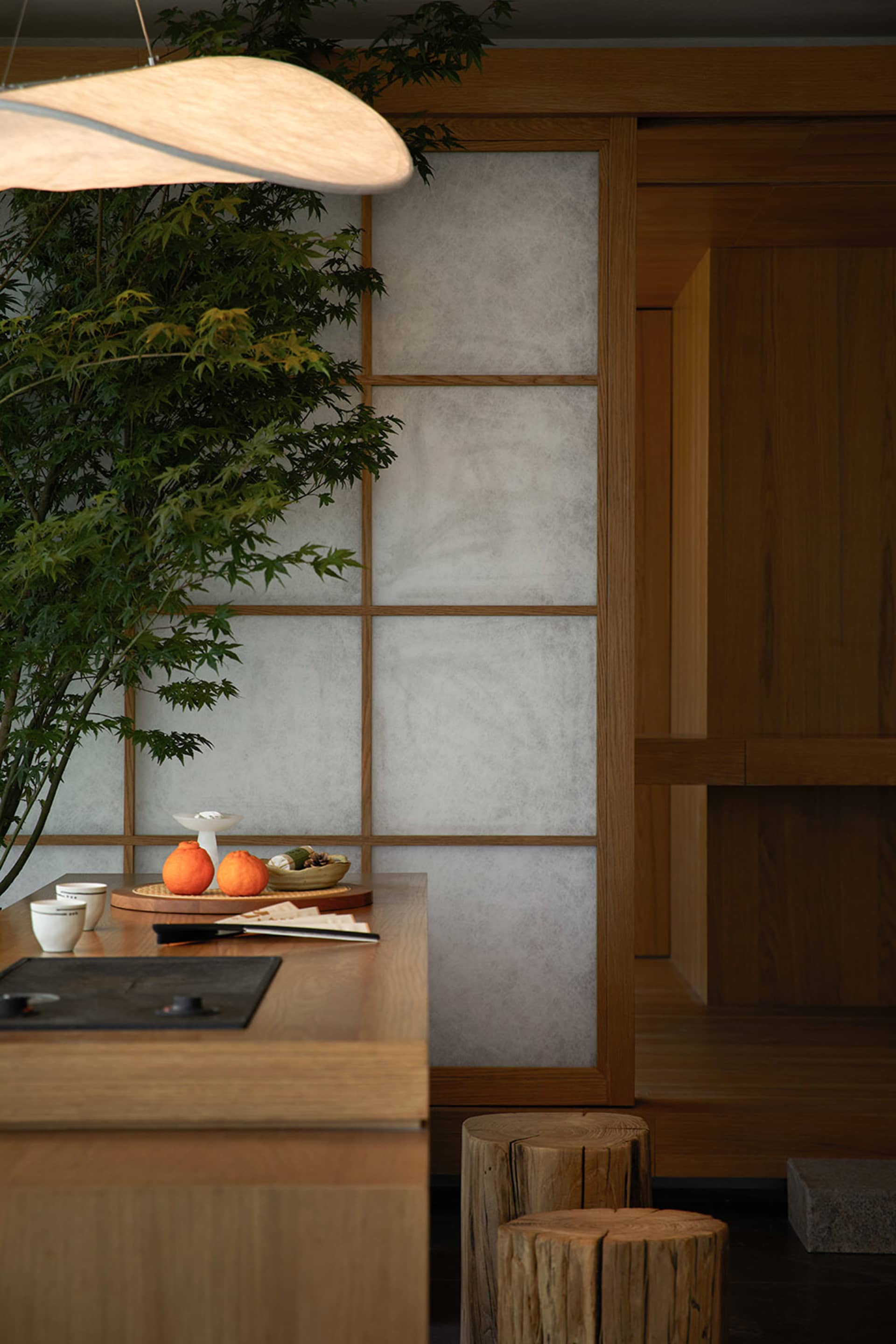A minimalist kitchen with paper walls and wooden cabinets features an orange fruit on a plate and a modern light fixture.