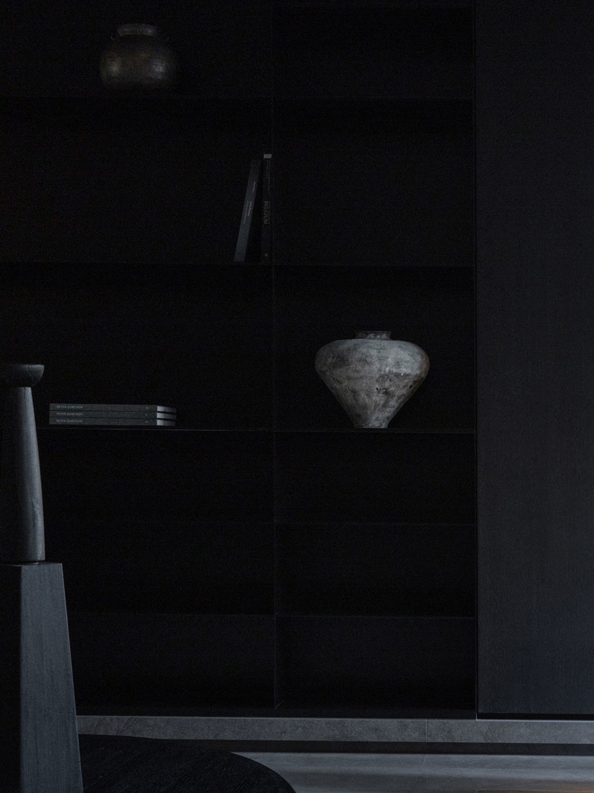 A modern black bookshelf with a ceramic vase on it.