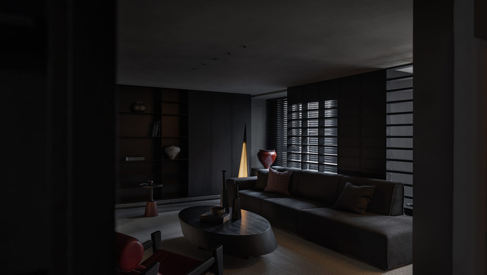 A minimalist living room with dark, sleek black furniture, a rug, and a light lamp.