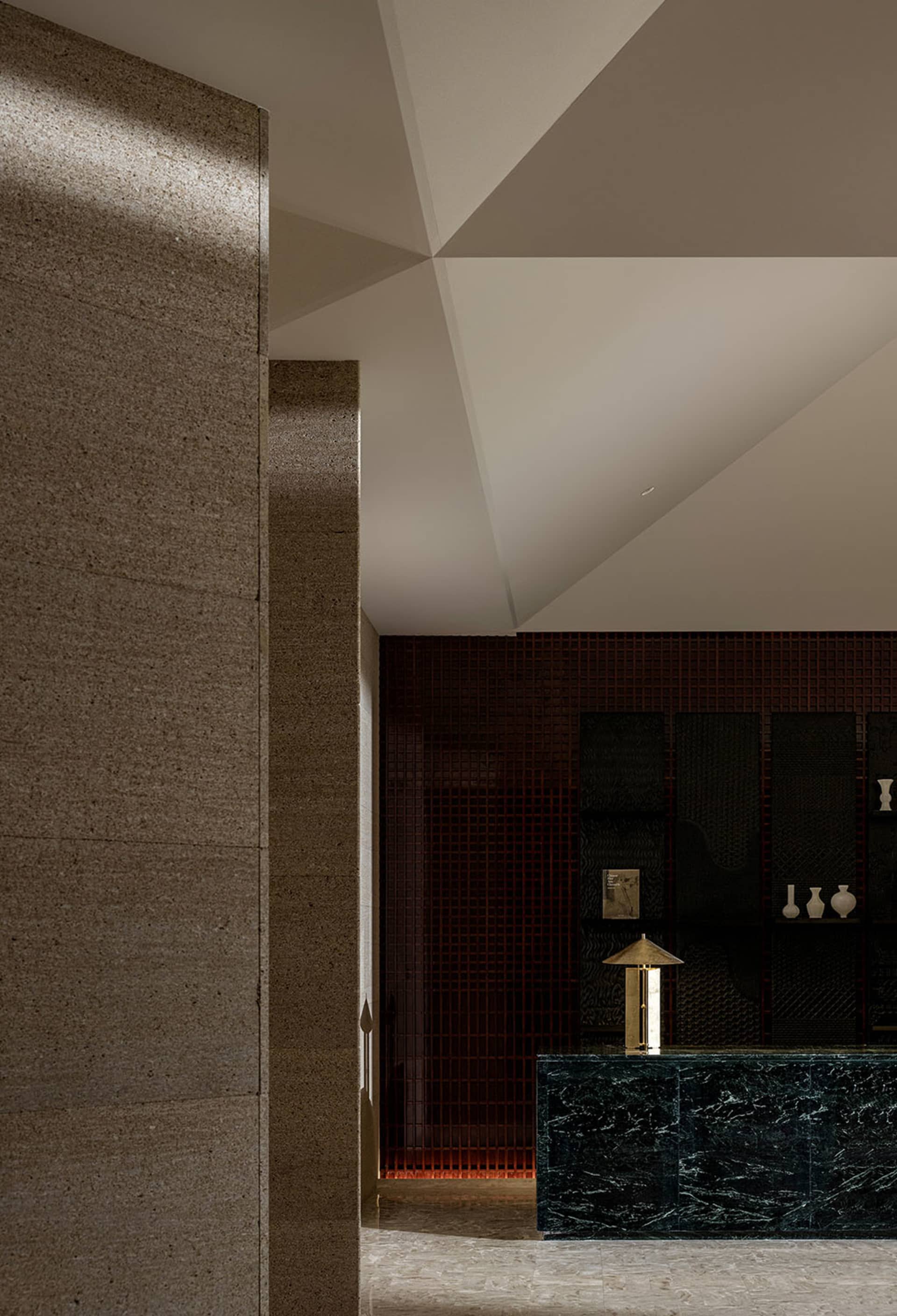 A modern lobby interior with a concrete wall and geometric ceiling design.