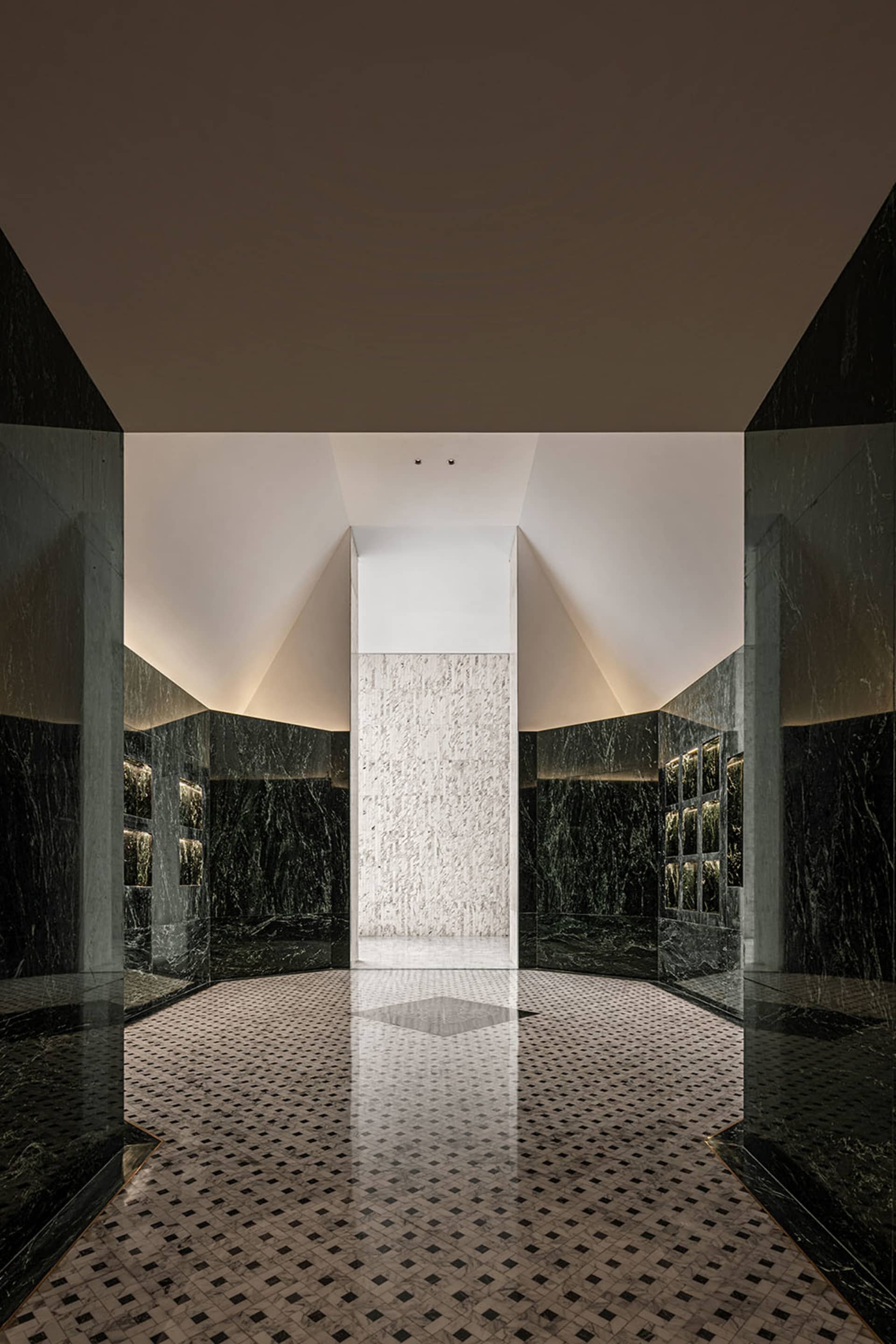 A modern marble hallway with geometric tiles and a white marble column in the center.