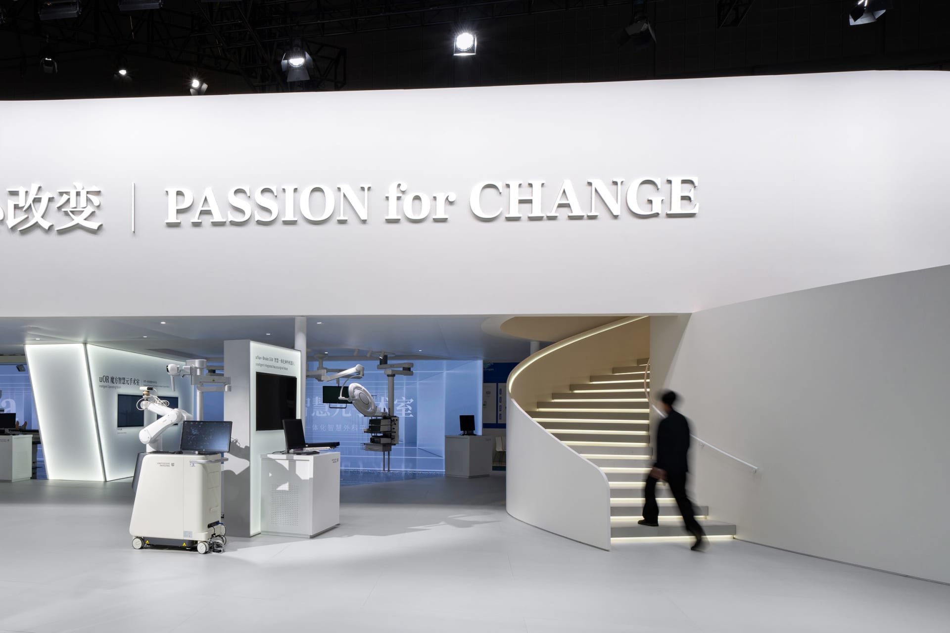 A minimalist exhibit hall with light concrete walls and a white spiral staircase.