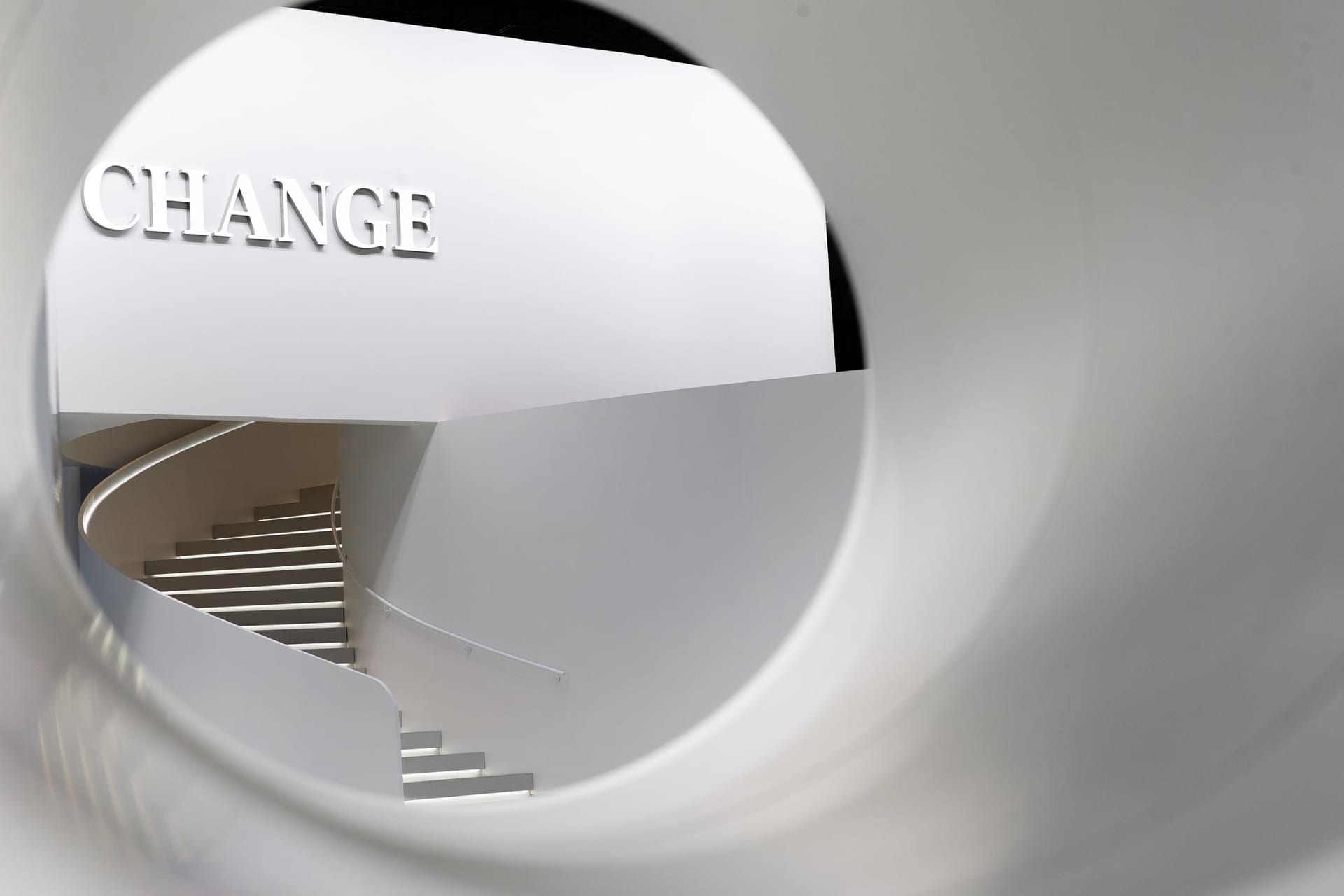 A minimalist staircase with white walls and steps, viewed through a circular opening.