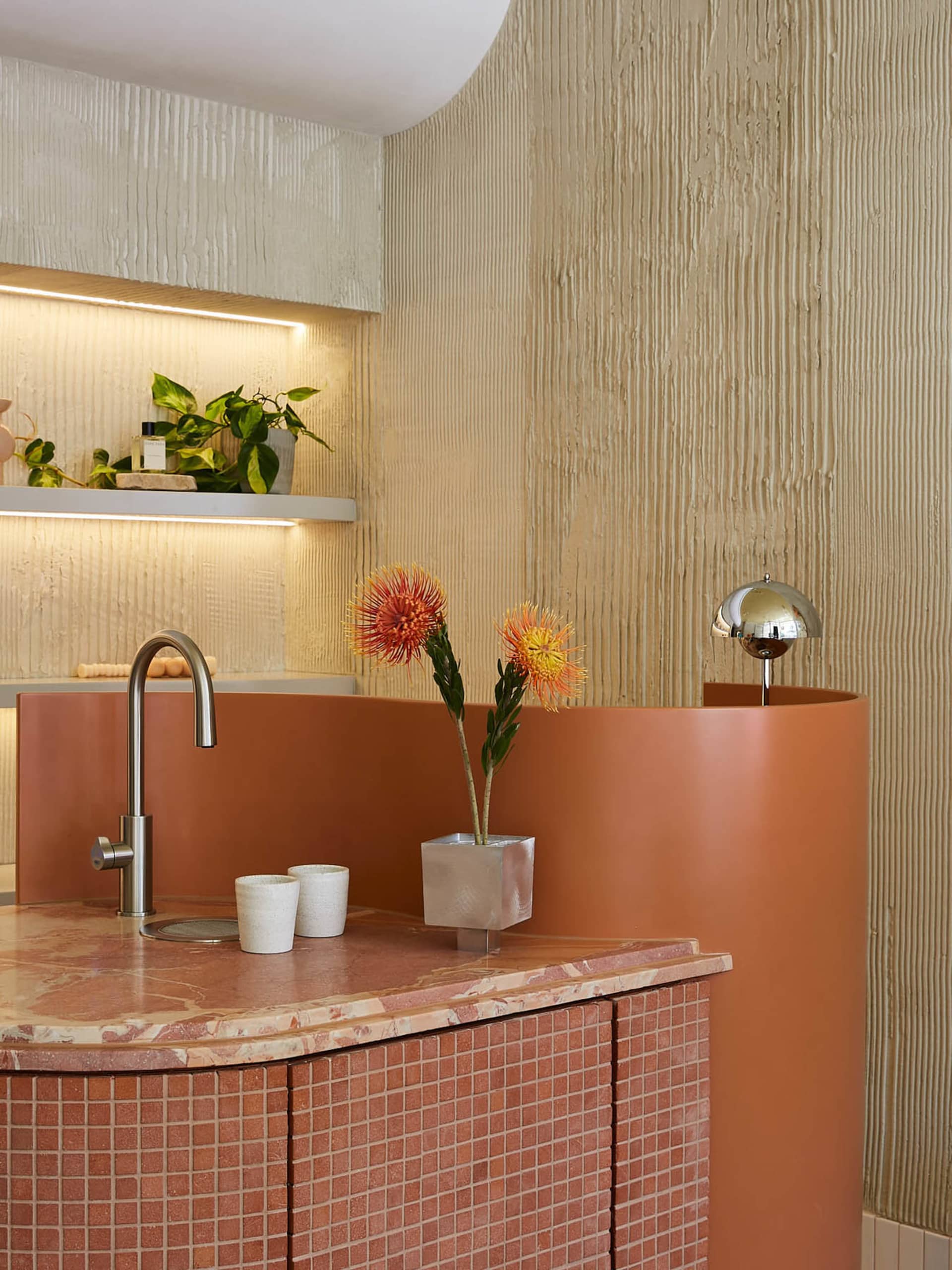 A modern bathroom featuring ceramic tile flooring and a terracotta-colored sink counter with a stainless steel faucet and pot
